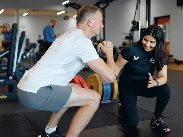 Personal trainer assessing client technique during gym exercise