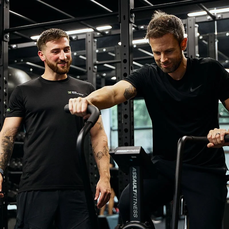 Level 2 gym instructor demonstrating proper exercise technique to client on gym equipment during practical training session