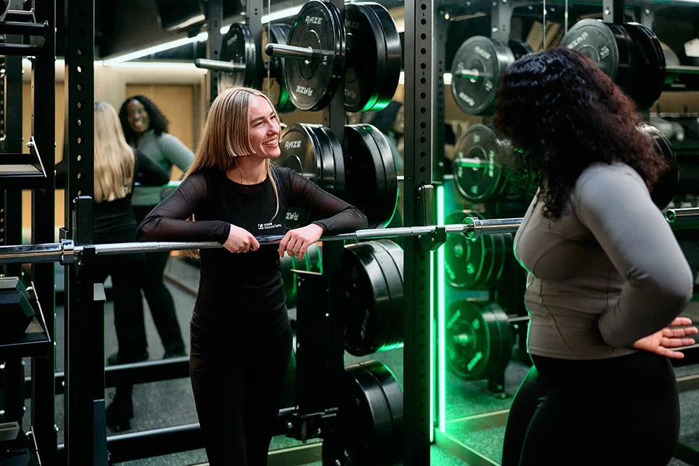 Personal trainer and client in a professional gym environment with barbell equipment