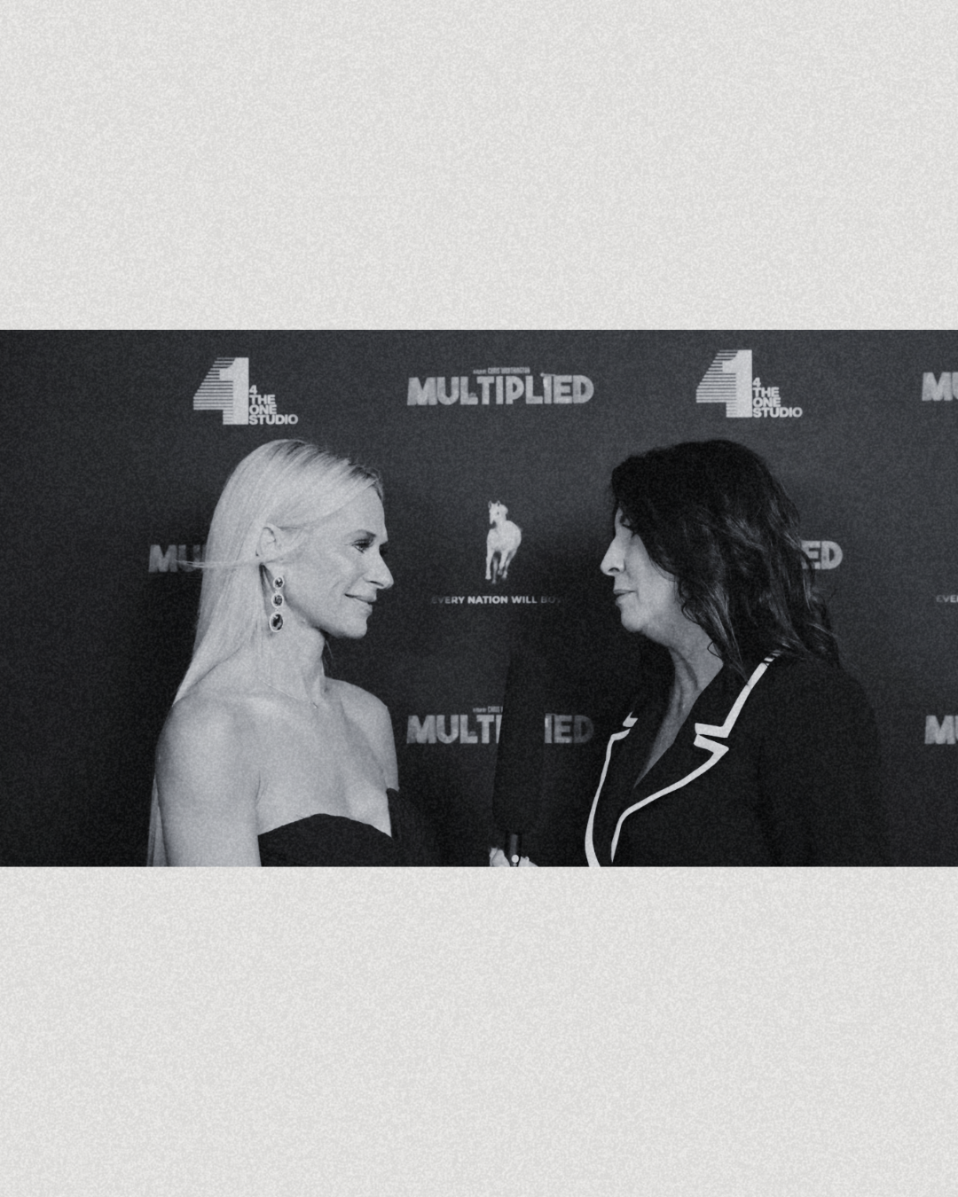 Two women standing face to face in front of a backdrop with logos, one with blonde hair and earrings, the other with dark hair and a blazer.