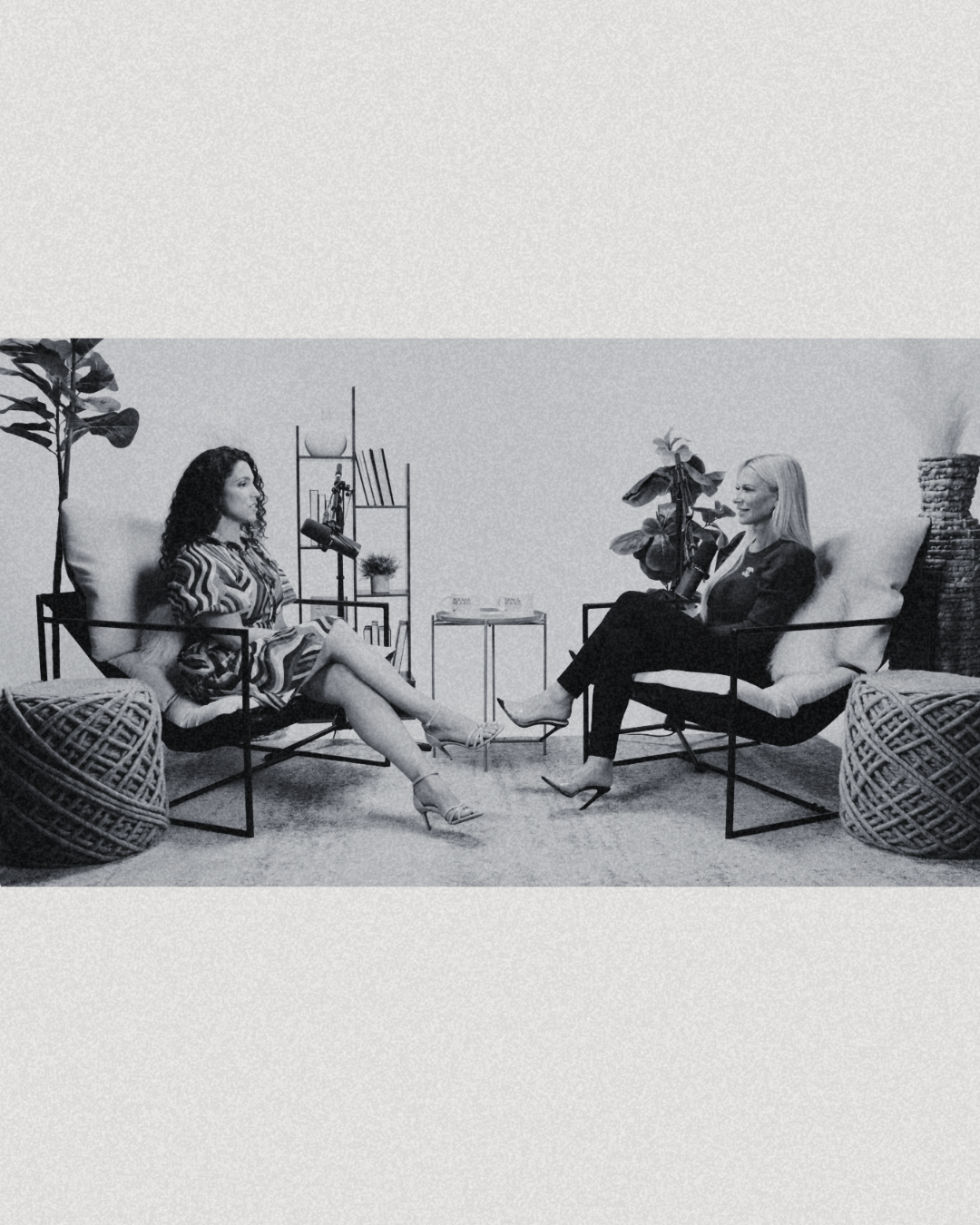 Two women sitting on armchairs facing each other in a modern room, engaged in conversation, with plants and decorative items in the background