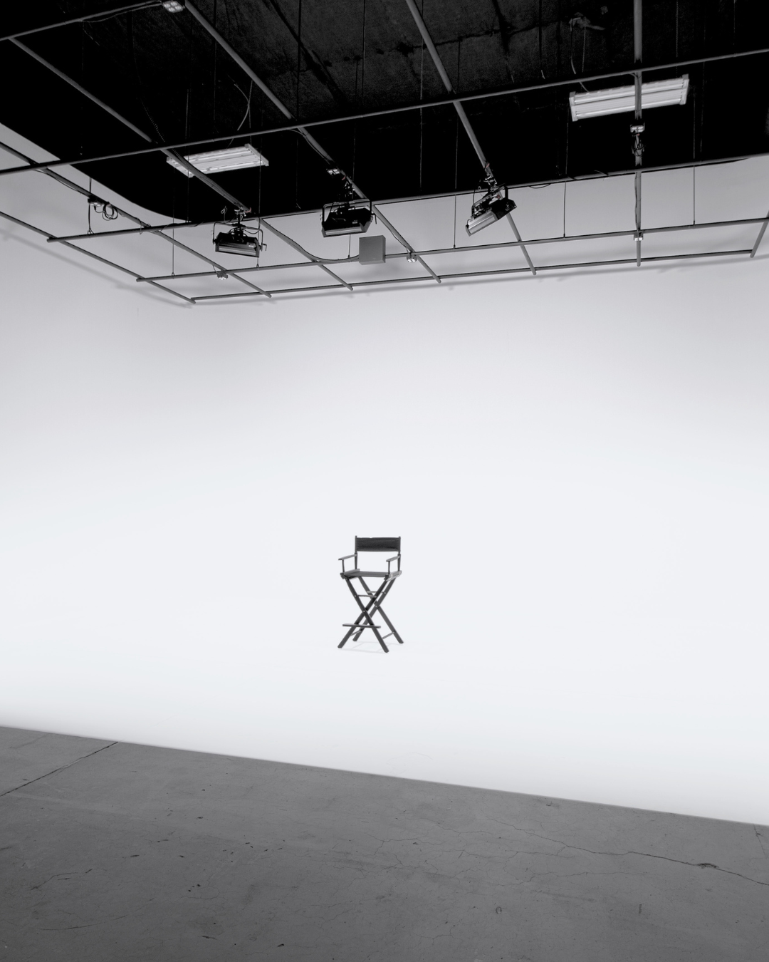 A director's chair centered on a white background in a photo studio, with overhead studio lights and rigging visible.