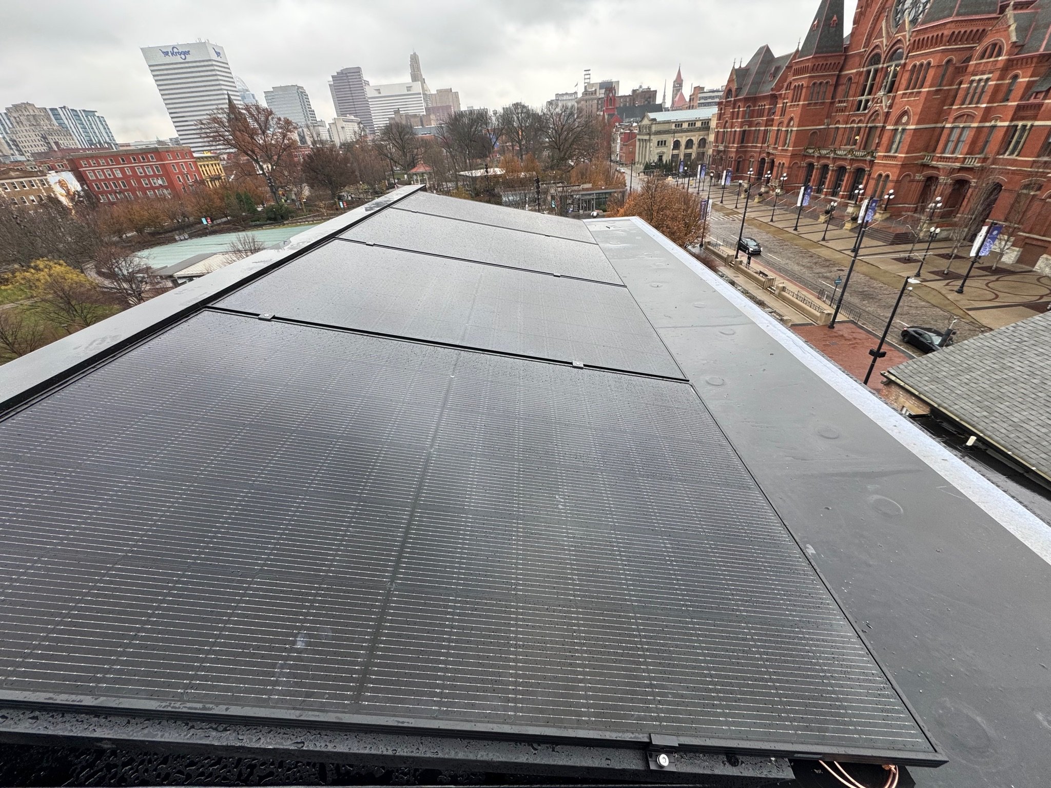 View of solar panels installed on a rooftop with city buildings and trees in the background