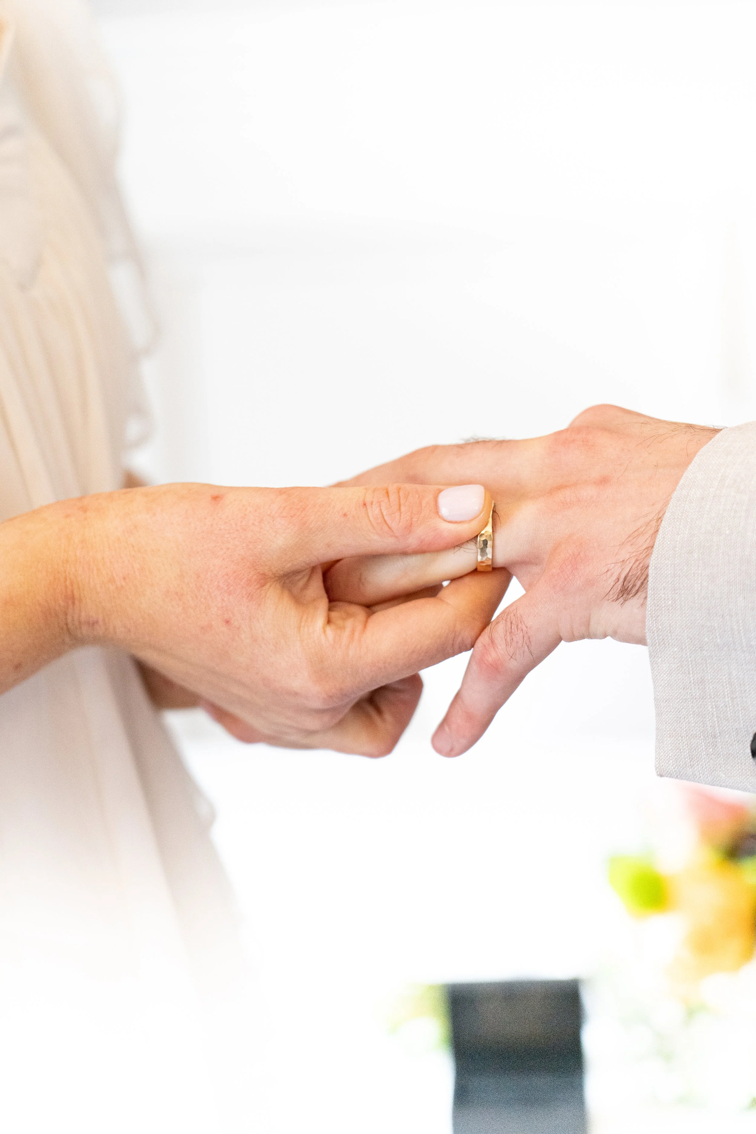 A person is placing a wedding ring on another person's finger during a wedding ceremony.