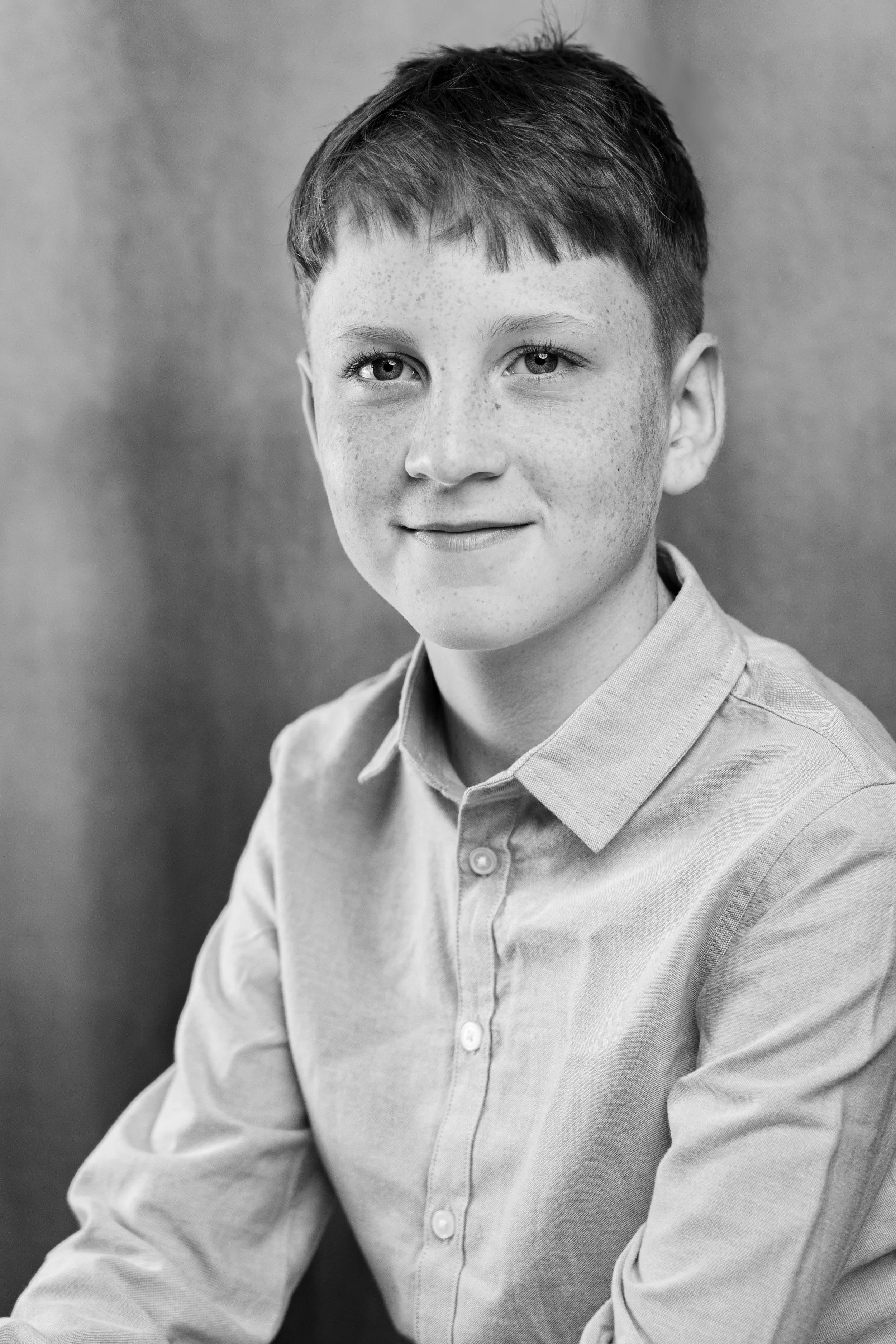A black and white portrait of a young boy with short hair and freckles, wearing a collared shirt, looking at the camera with a slight smile.
