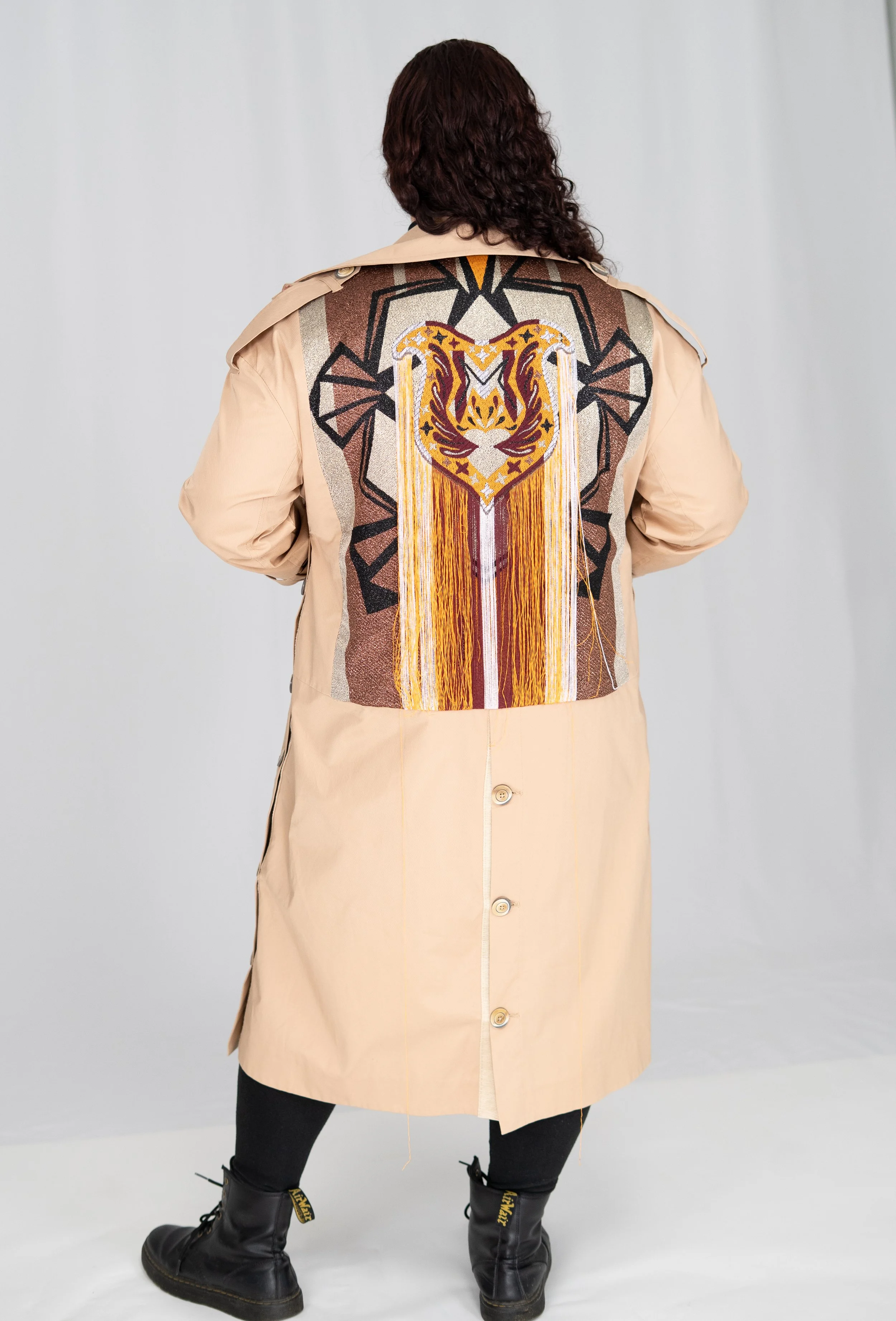 A person wearing a beige trench coat with a colorful embroidered tiger face design on the back.