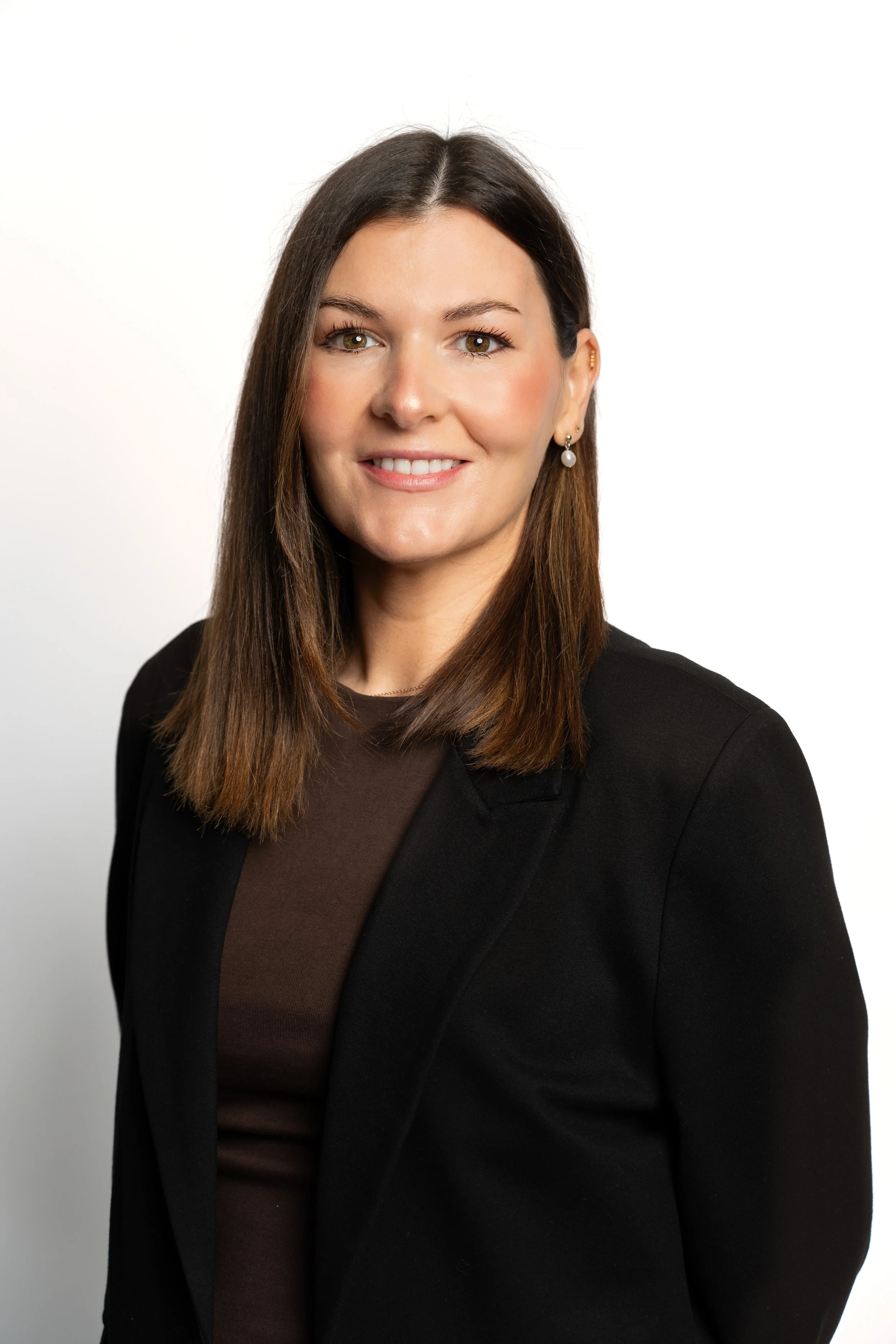 Professional woman with shoulder-length brown hair, wearing a black blazer and a brown top, smiling against a white background.