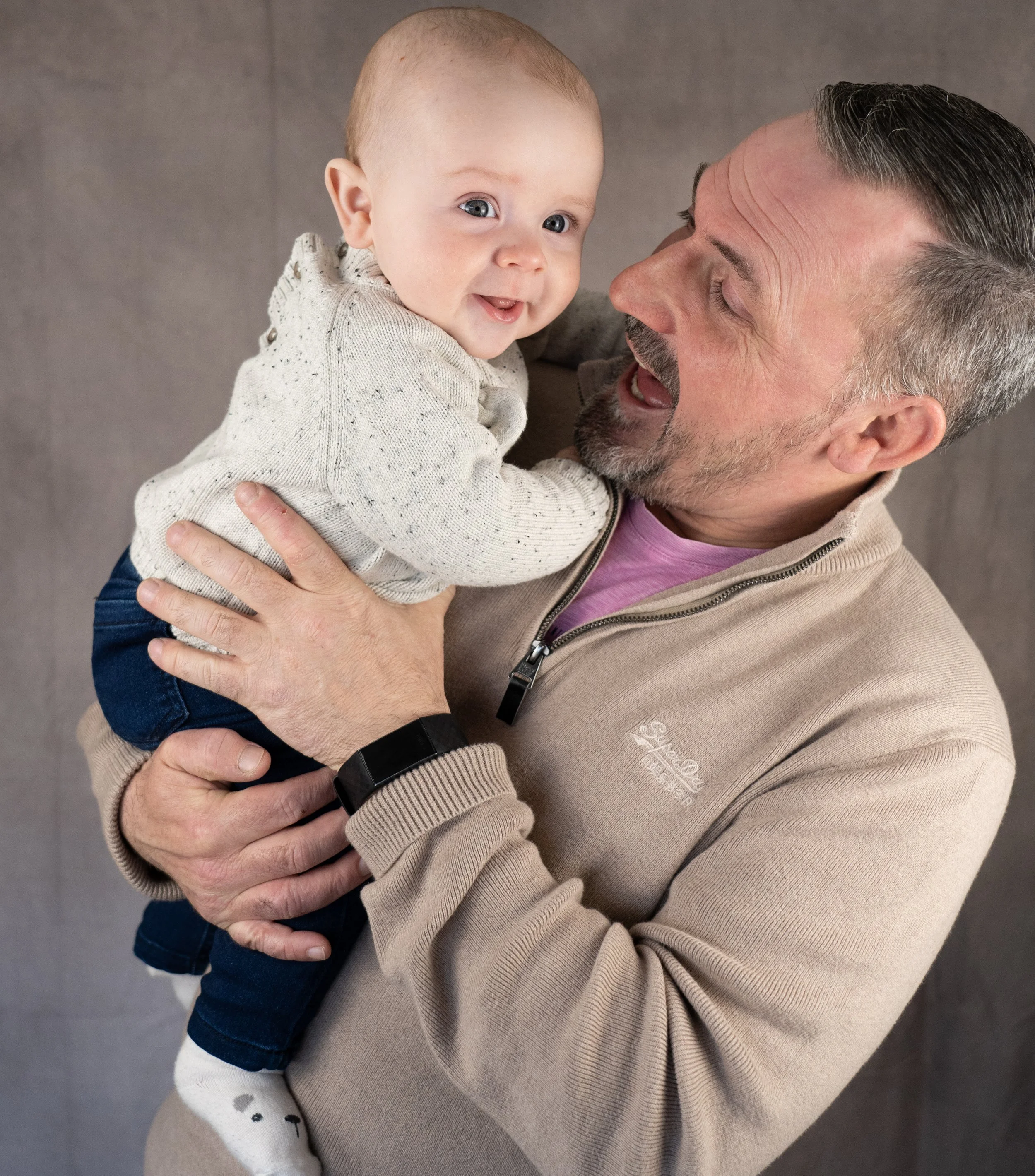 A man holding a smiling baby girl, both looking at the camera.