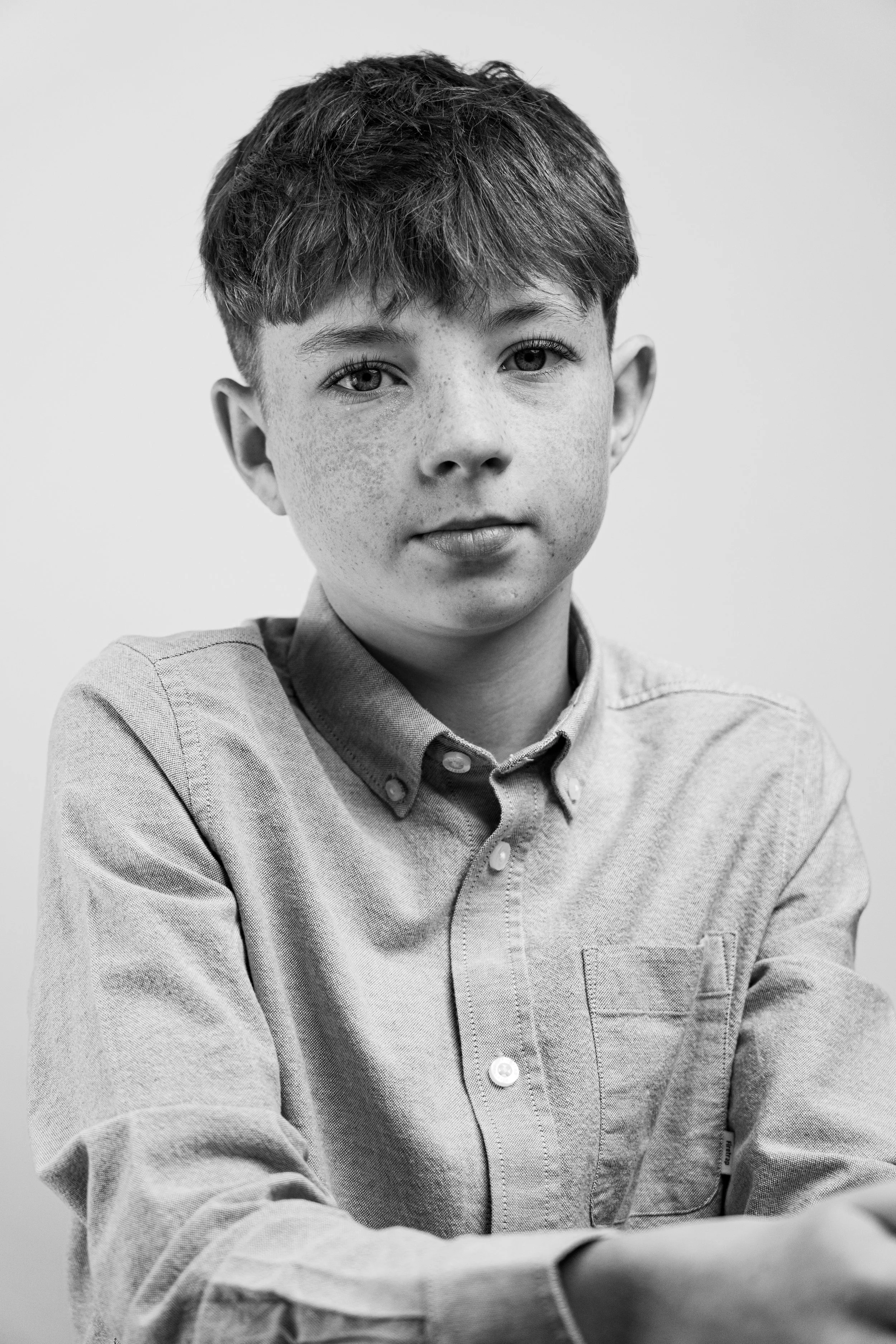 Black and white portrait of a young boy with short, slightly tousled hair, freckles, and a serious expression, wearing a button-up shirt with the sleeves rolled up.