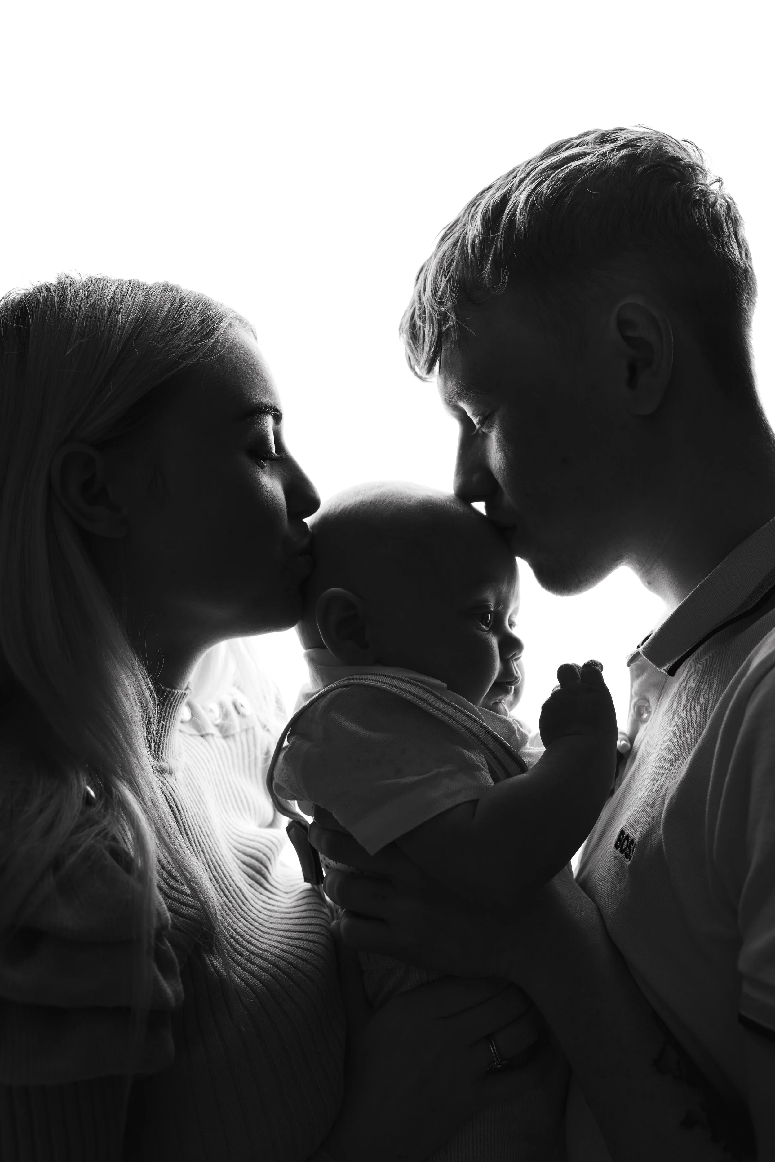 Silhouette of a family, with the mother and father kissing their baby, who is facing them.