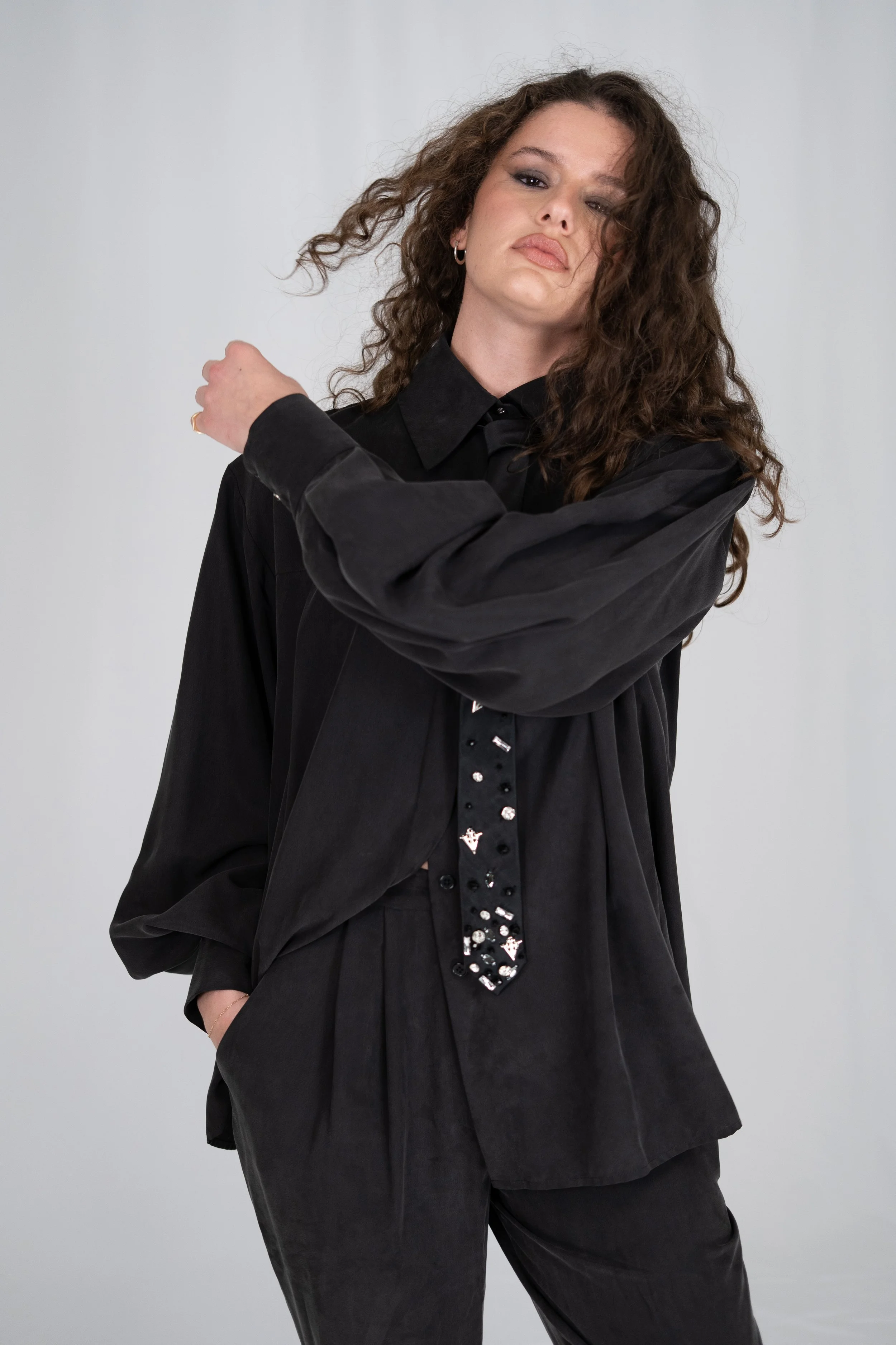 Woman with curly hair wearing black outfit, looking confidently at the camera against a plain light background.