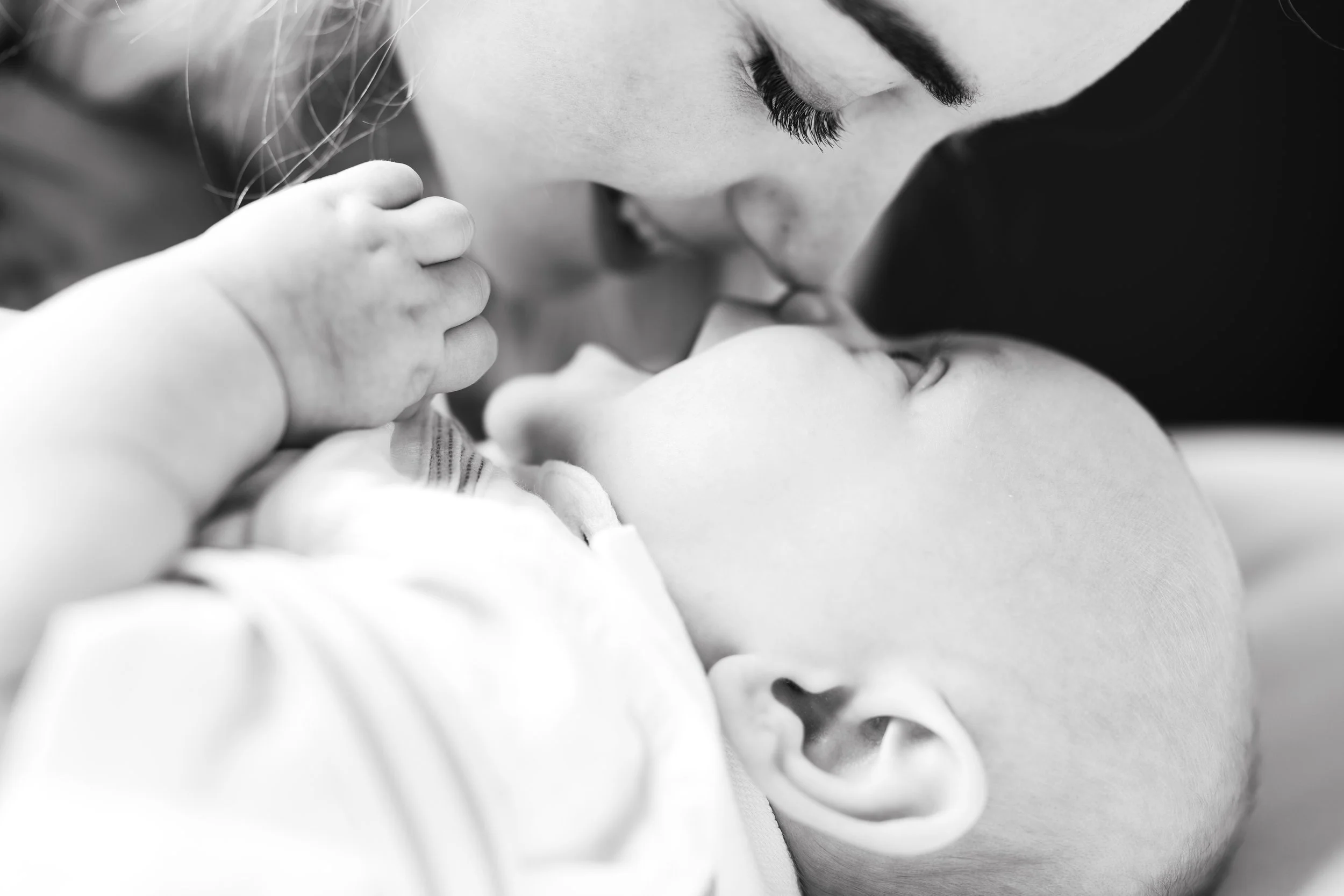 A woman and a young child sharing a tender moment, with the woman kissing the child's forehead, in black and white.