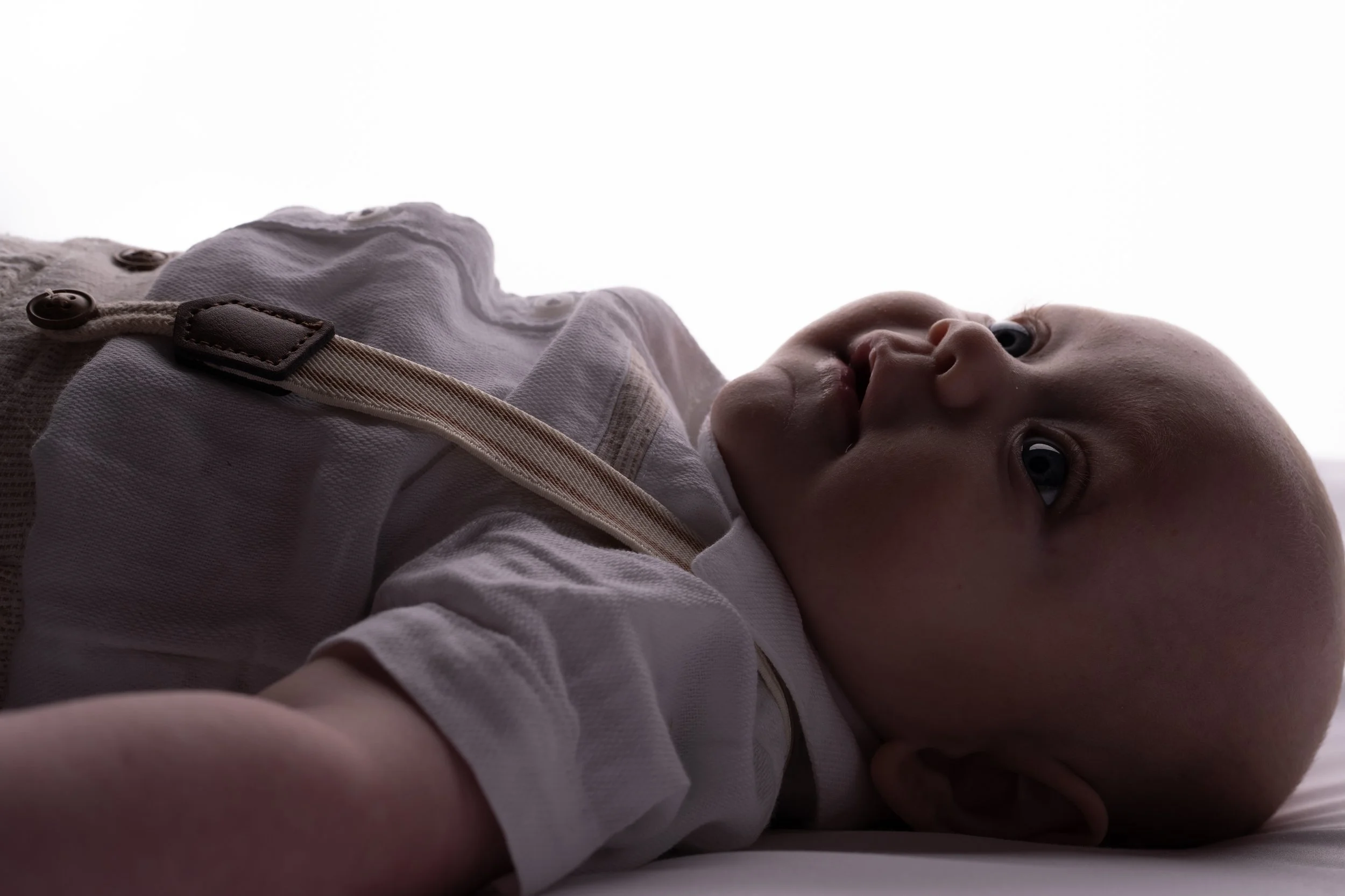 Close-up of a baby lying down, looking to the side, with bright backlighting