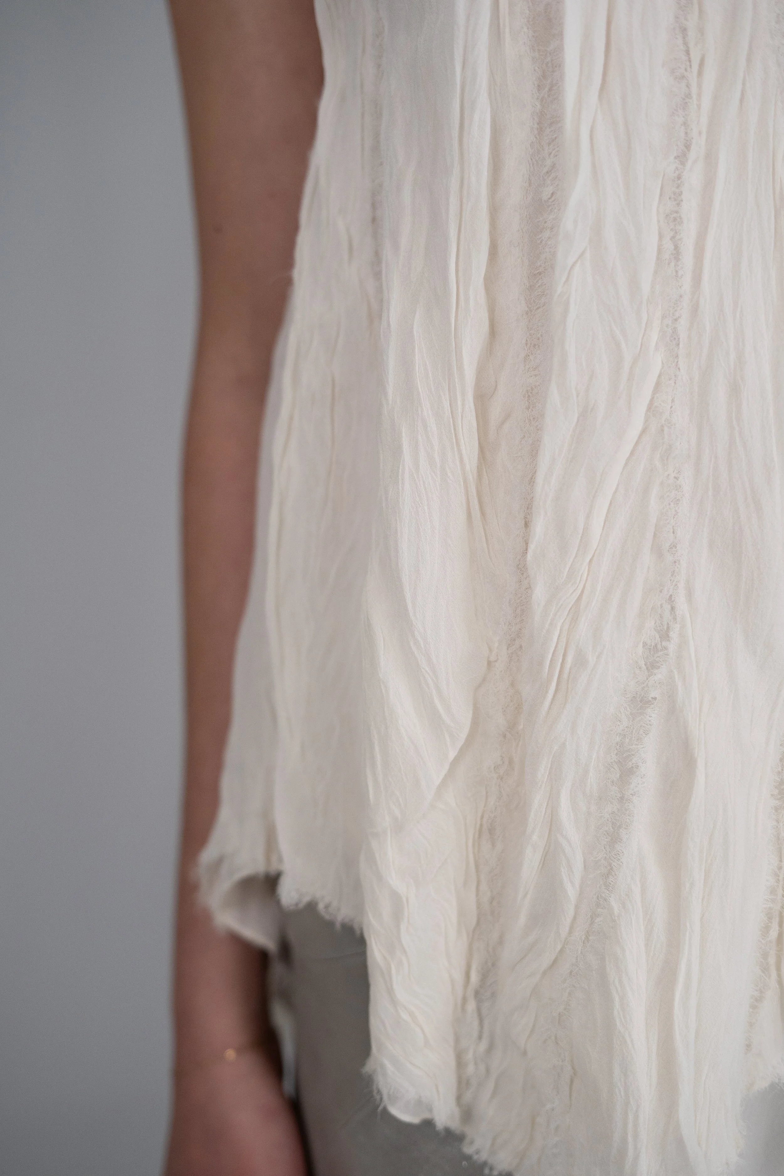Close-up of a person wearing a flowing, off-white textured dress beside a plain gray background.