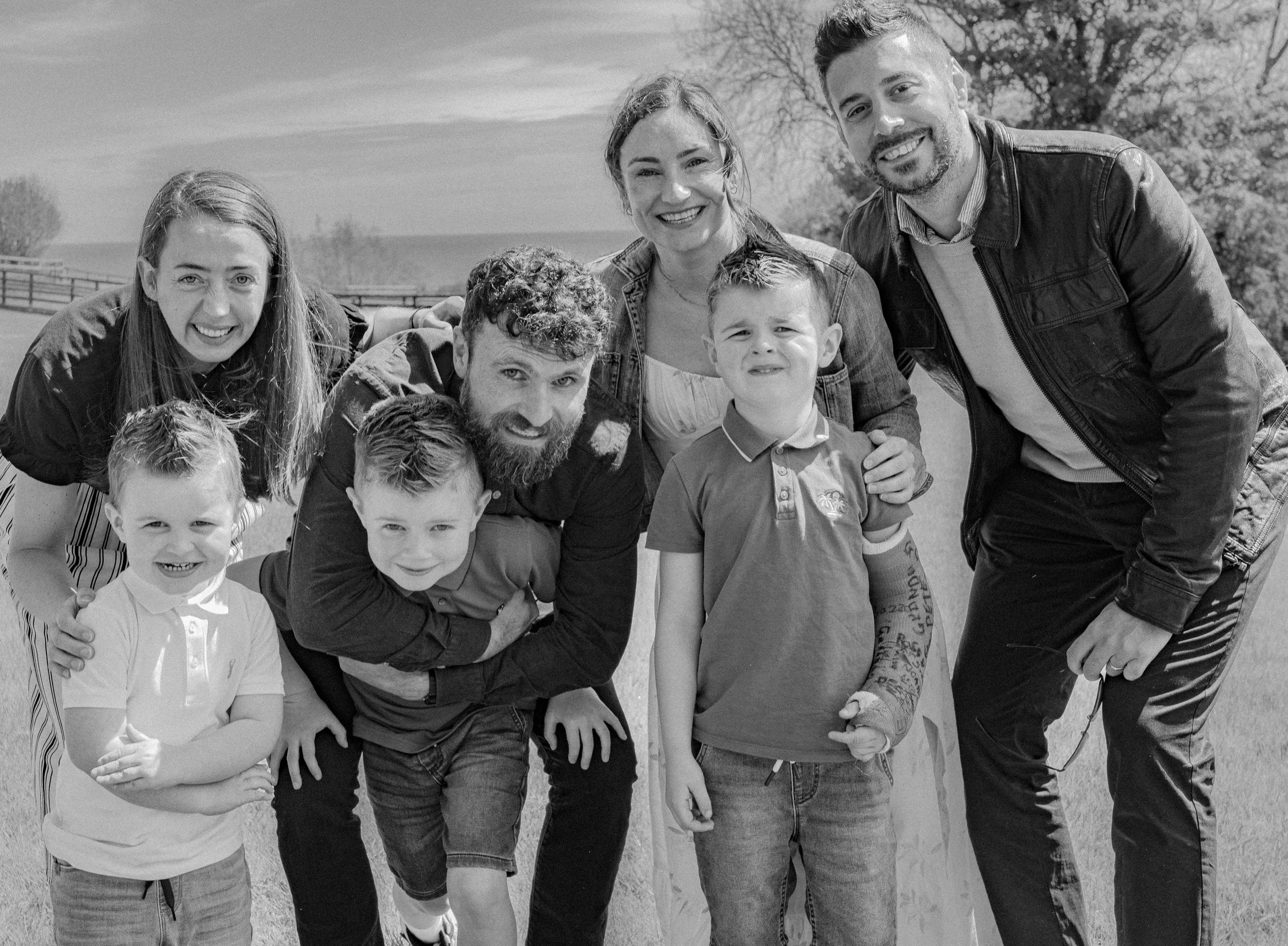 A black and white photo of a happy family outdoors, consisting of three adults and four children, smiling and posing for the camera.