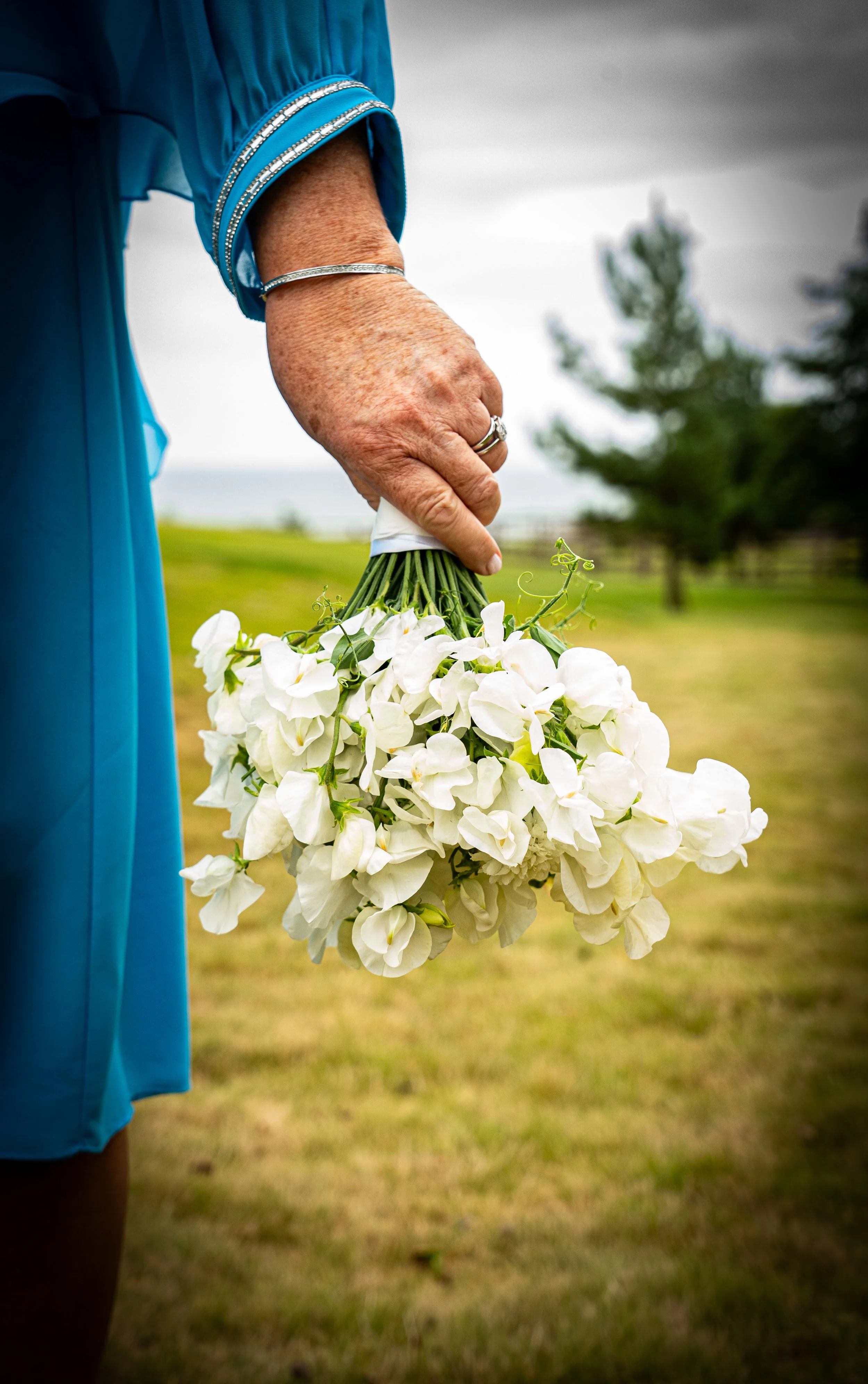 A woman in a blue dress holding a bouquet of white flowers outdoors on a cloudy day.