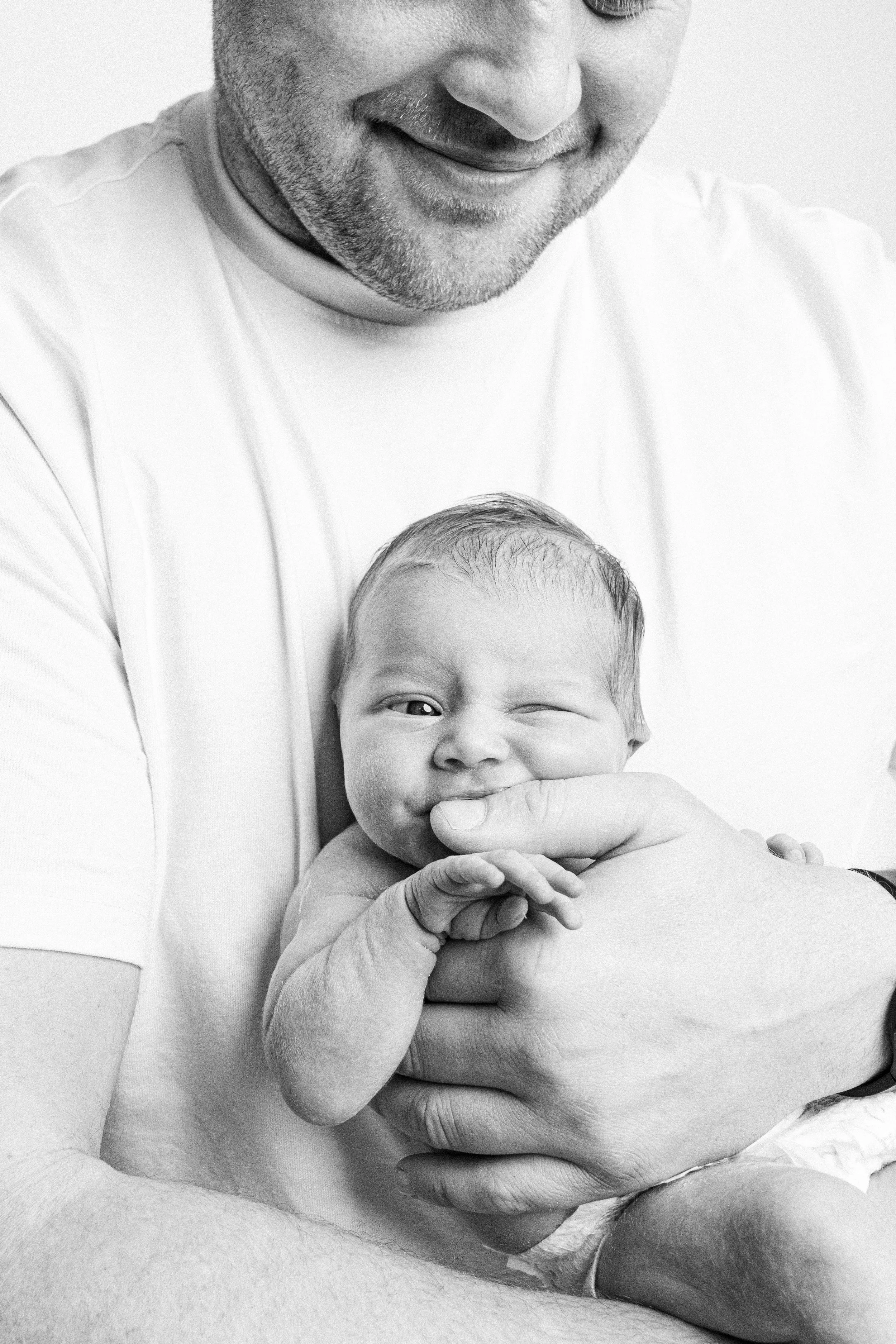 A man holding a newborn baby, the man smiling down at the baby in black and white.