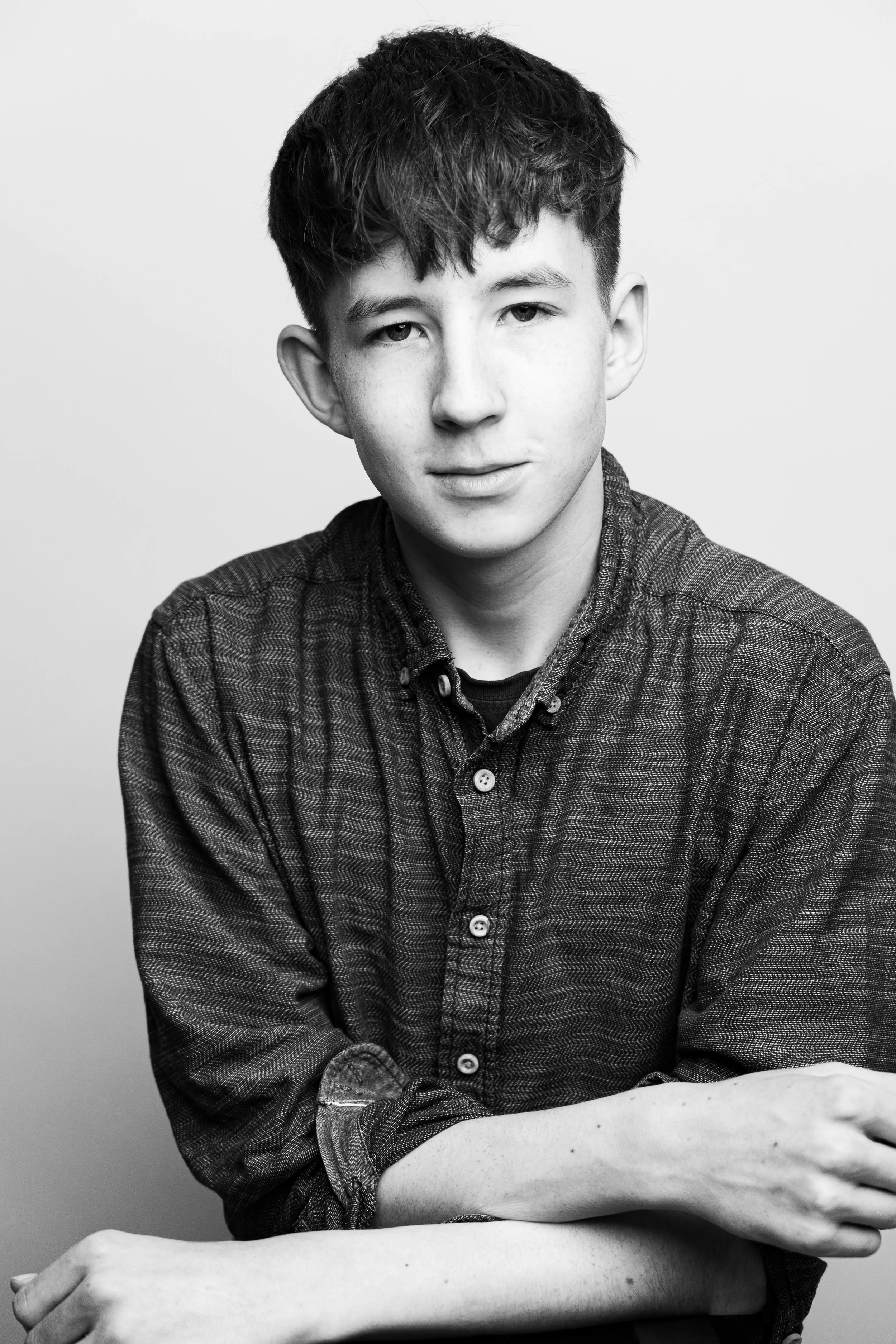 Black and white portrait of a young man with short, dark hair, wearing a button-up shirt with rolled-up sleeves, looking at the camera with a neutral expression.