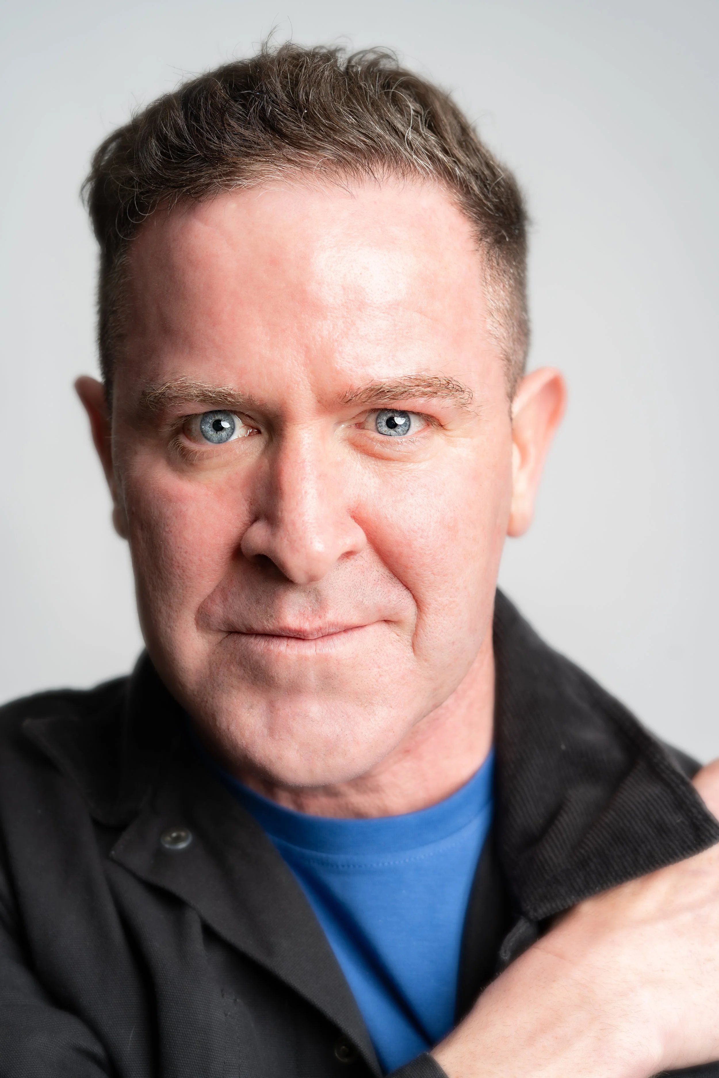 Headshot of a middle-aged man with short, dark hair and blue eyes, wearing a black jacket over a blue shirt, looking at the camera with a confident expression.