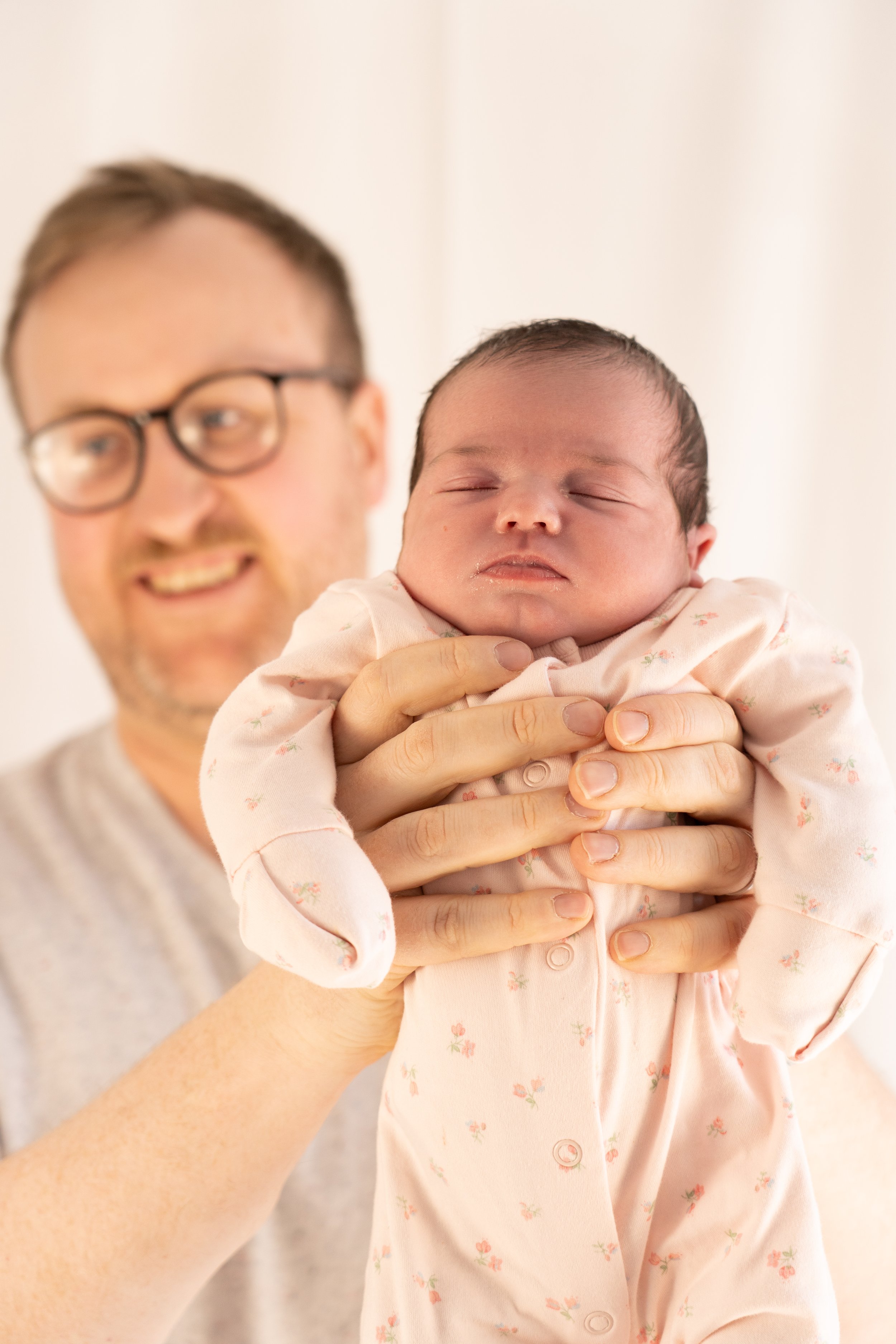 A man holding a sleeping baby girl in a pink floral onesie.