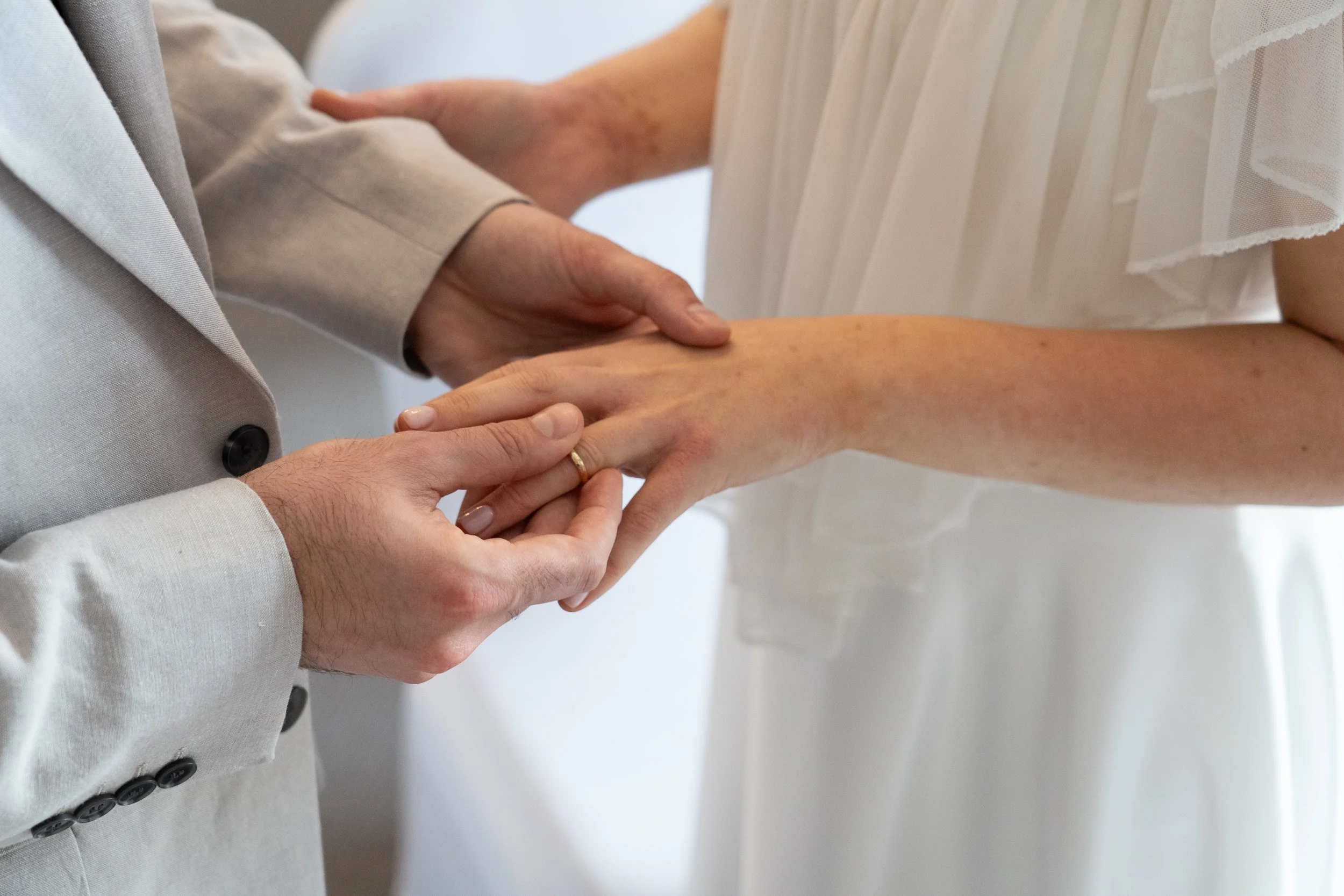 A couple exchanges wedding rings during a ceremony, with one person placing a gold band on the other's finger.