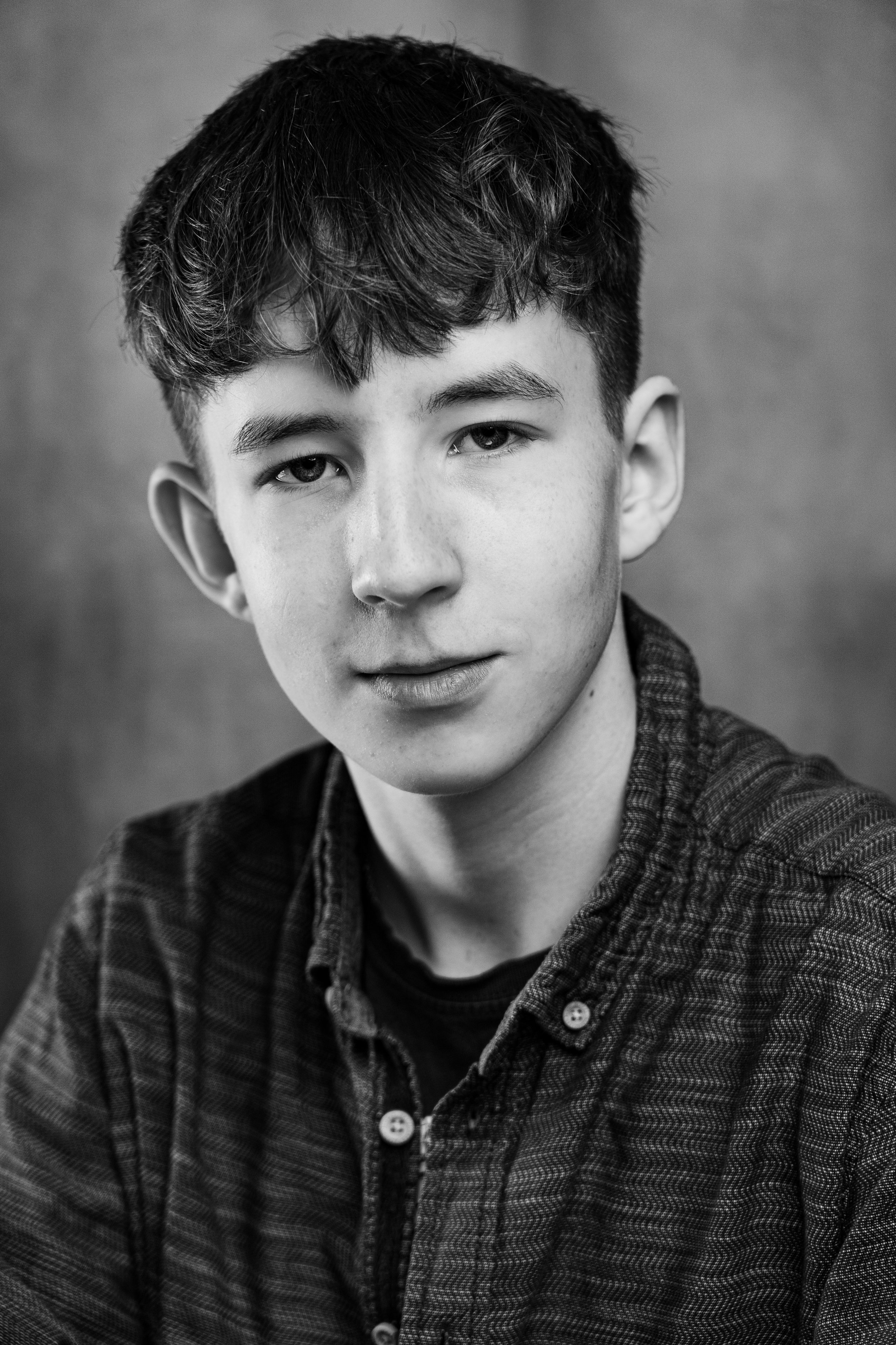 Portrait of a young man with wavy hair, wearing a patterned shirt, looking at the camera, in black and white.