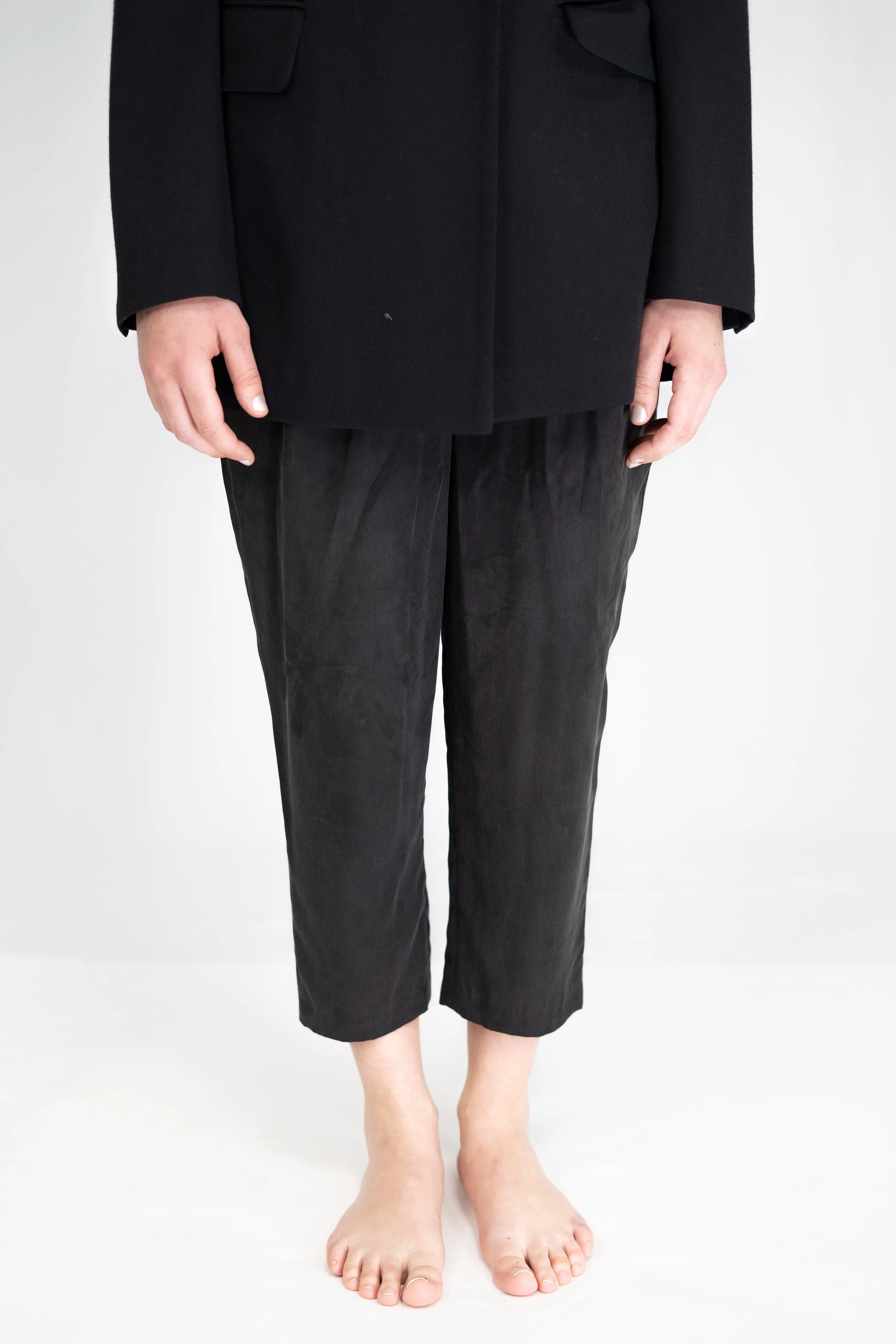 Person standing barefoot wearing black pants and a black coat.