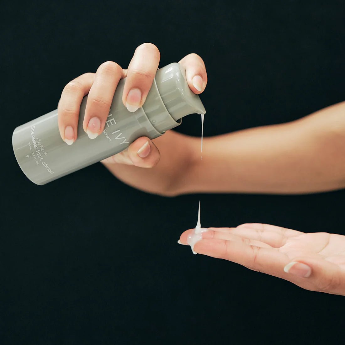A person dispensing lotion from a grey bottle onto their finger.