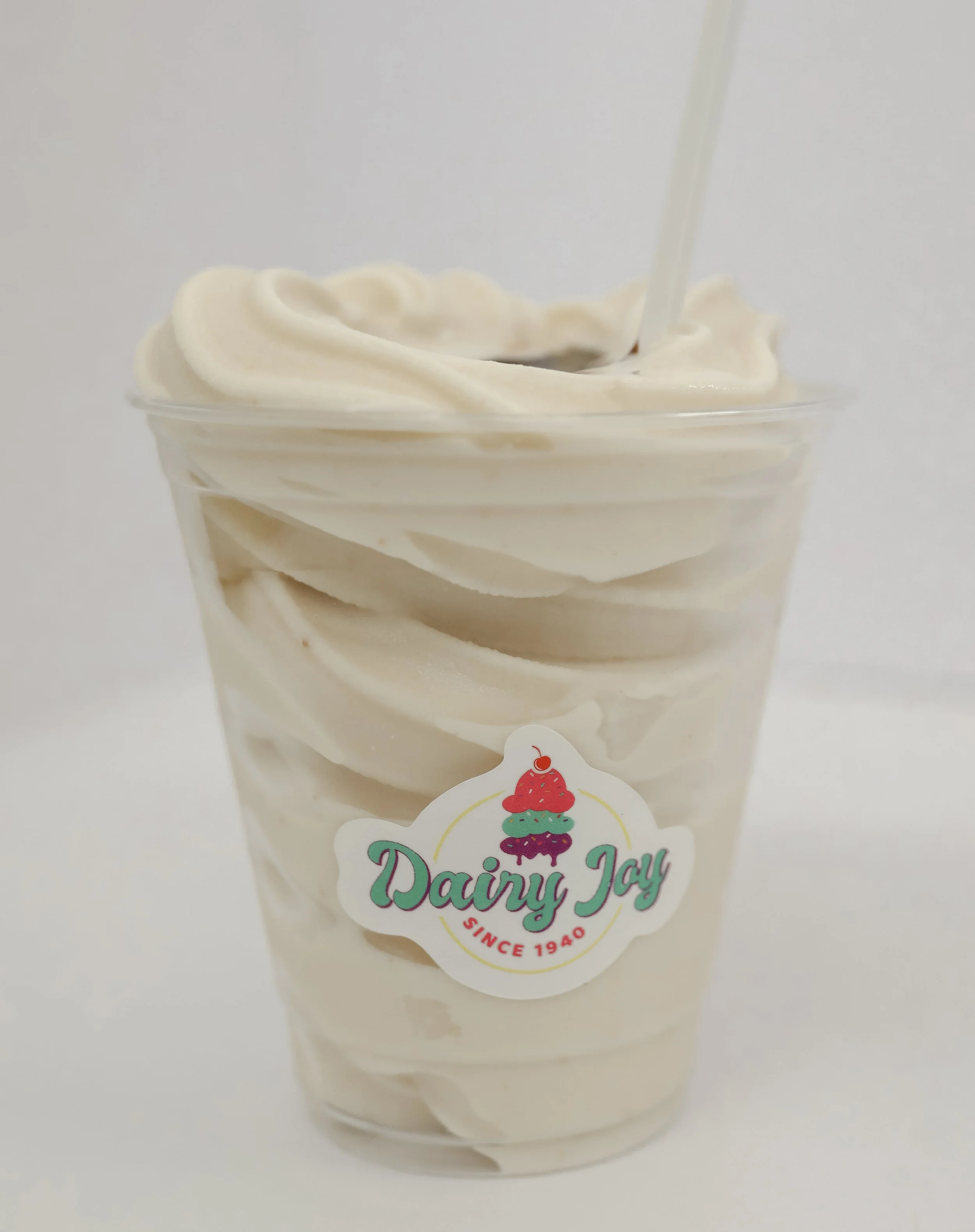 A clear plastic cup filled with soft serve vanilla ice cream, with a label that reads 'Dairy Joy Since 1940' and a colorful ice cream cone graphic.