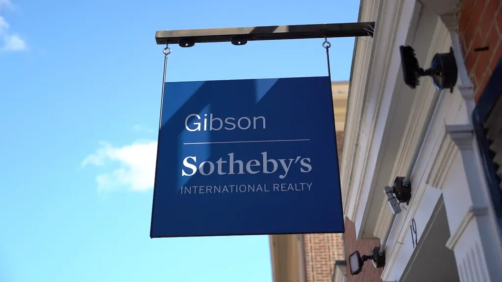 A blue sign hanging outside a building that reads "Gibson Sotheby's International Realty."