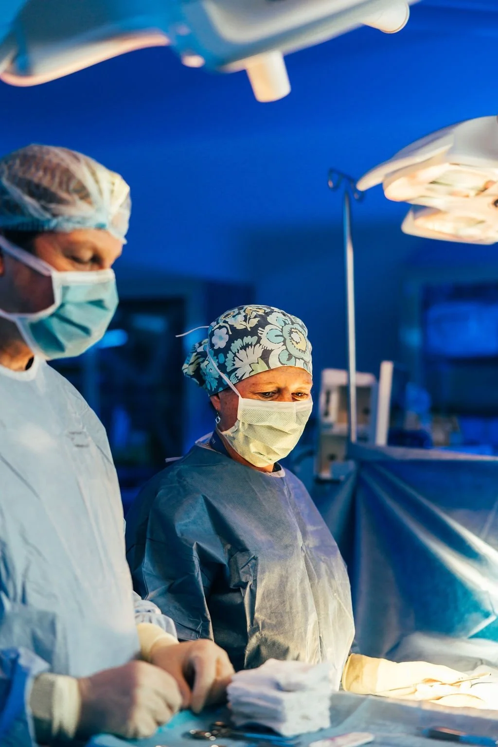 Surgeons in an operating room wearing scrubs, masks, and surgical caps during a procedure.