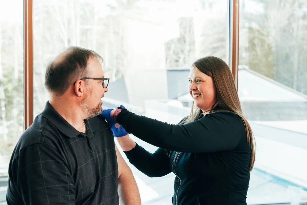 A woman is giving a man a vaccination in a clinical setting with large windows and natural light.