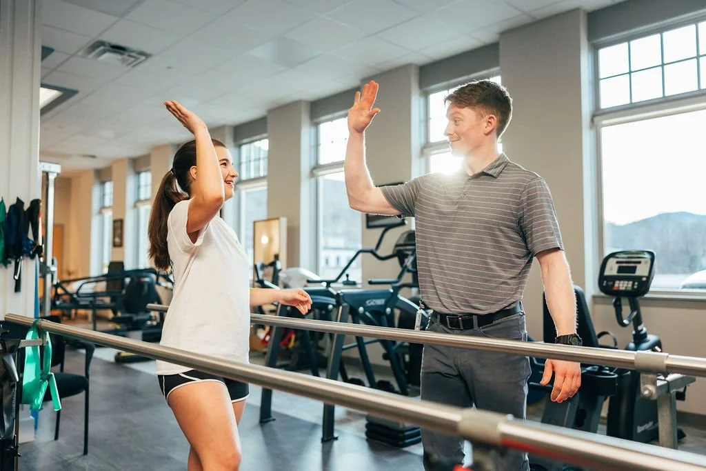 A man and a woman in a gym giving each other high fives.