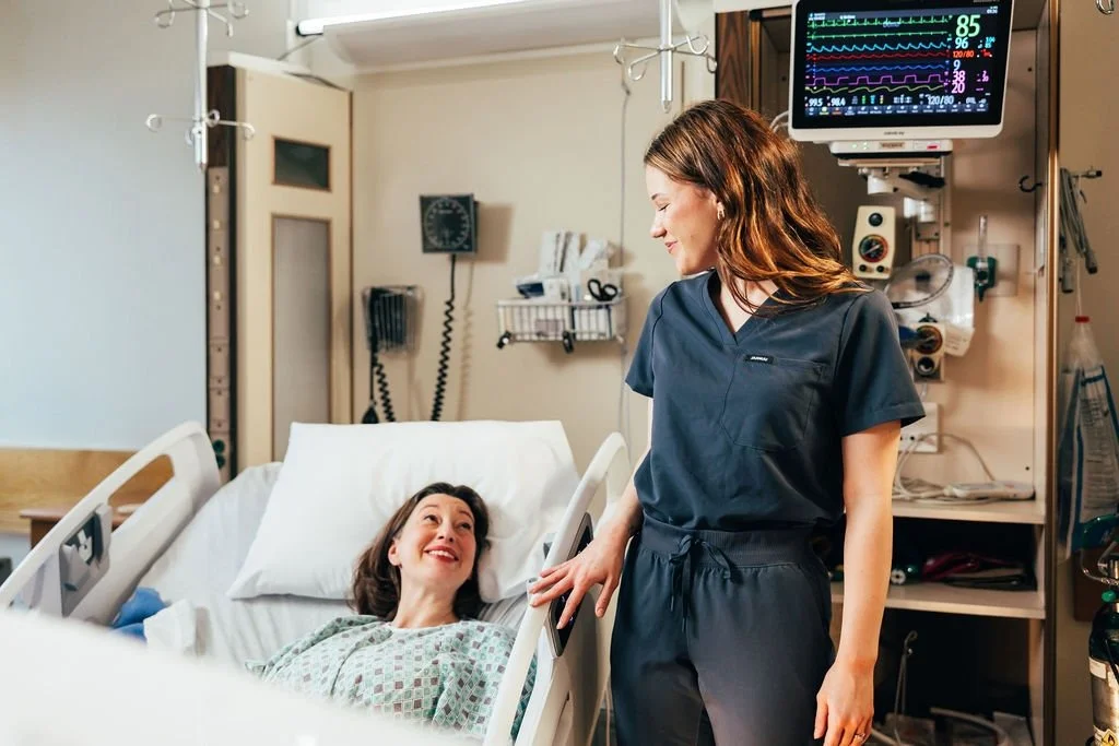 A nurse talking to a woman lying in a hospital bed in a hospital room.