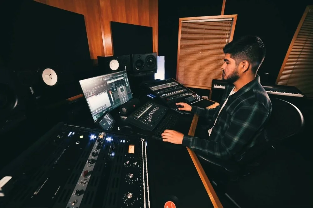Man working in a music studio with mixing consoles, monitors, and audio equipment.