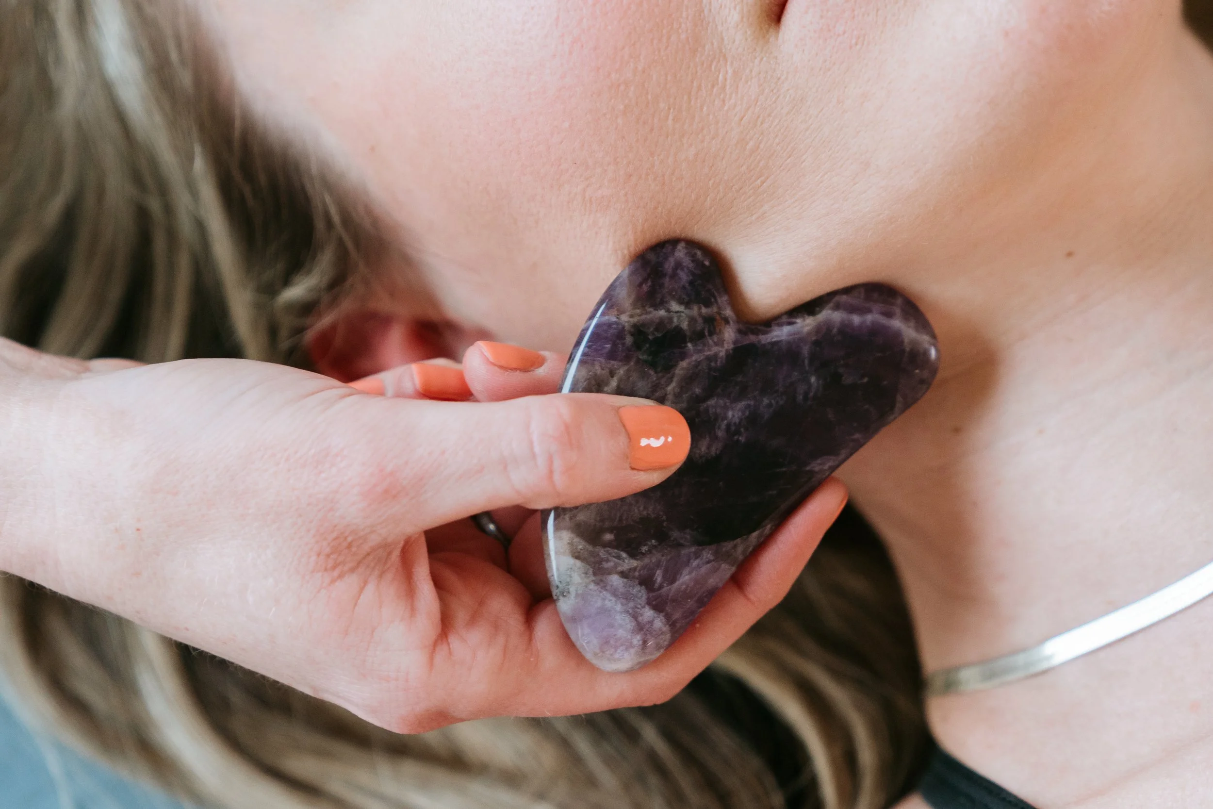 A person holding a large, heart-shaped, dark purple stone close to their face.