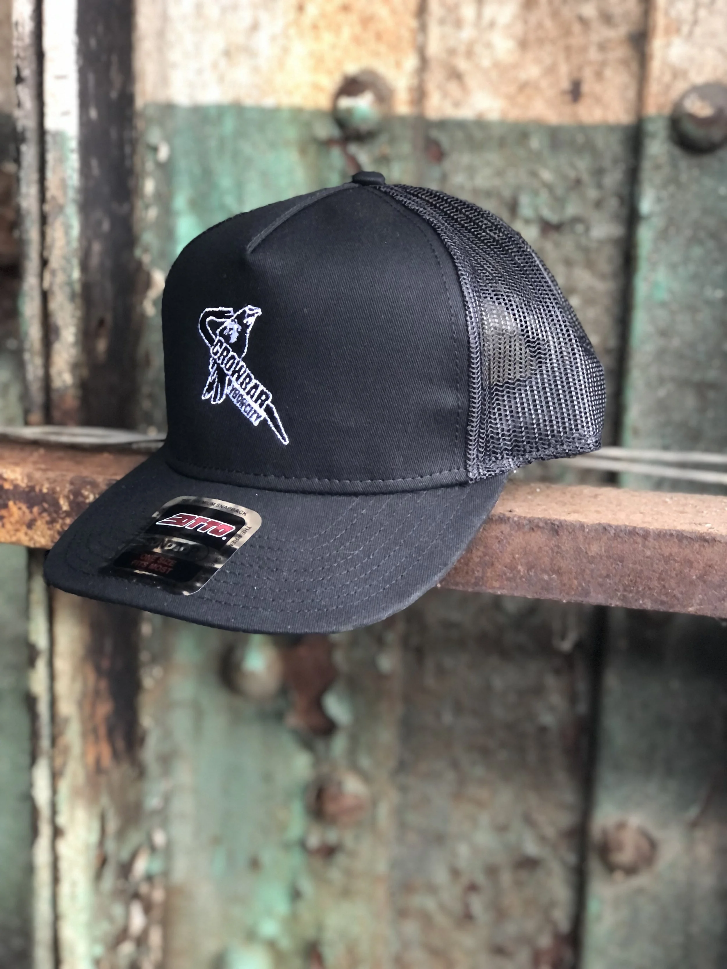 A black trucker hat with the Crowbar music venue logo on an industrial rail and metal background.