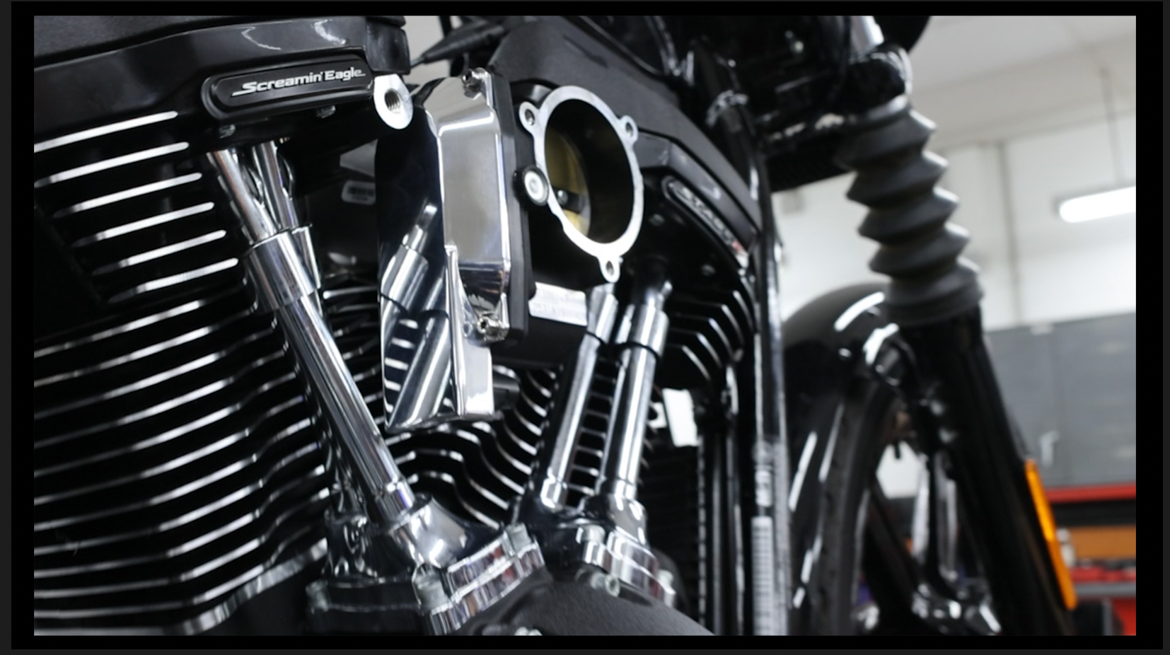 Close-up of a black motorcycle engine with shiny chrome custom NAMZ throttle body coverand an open section revealing internal parts.