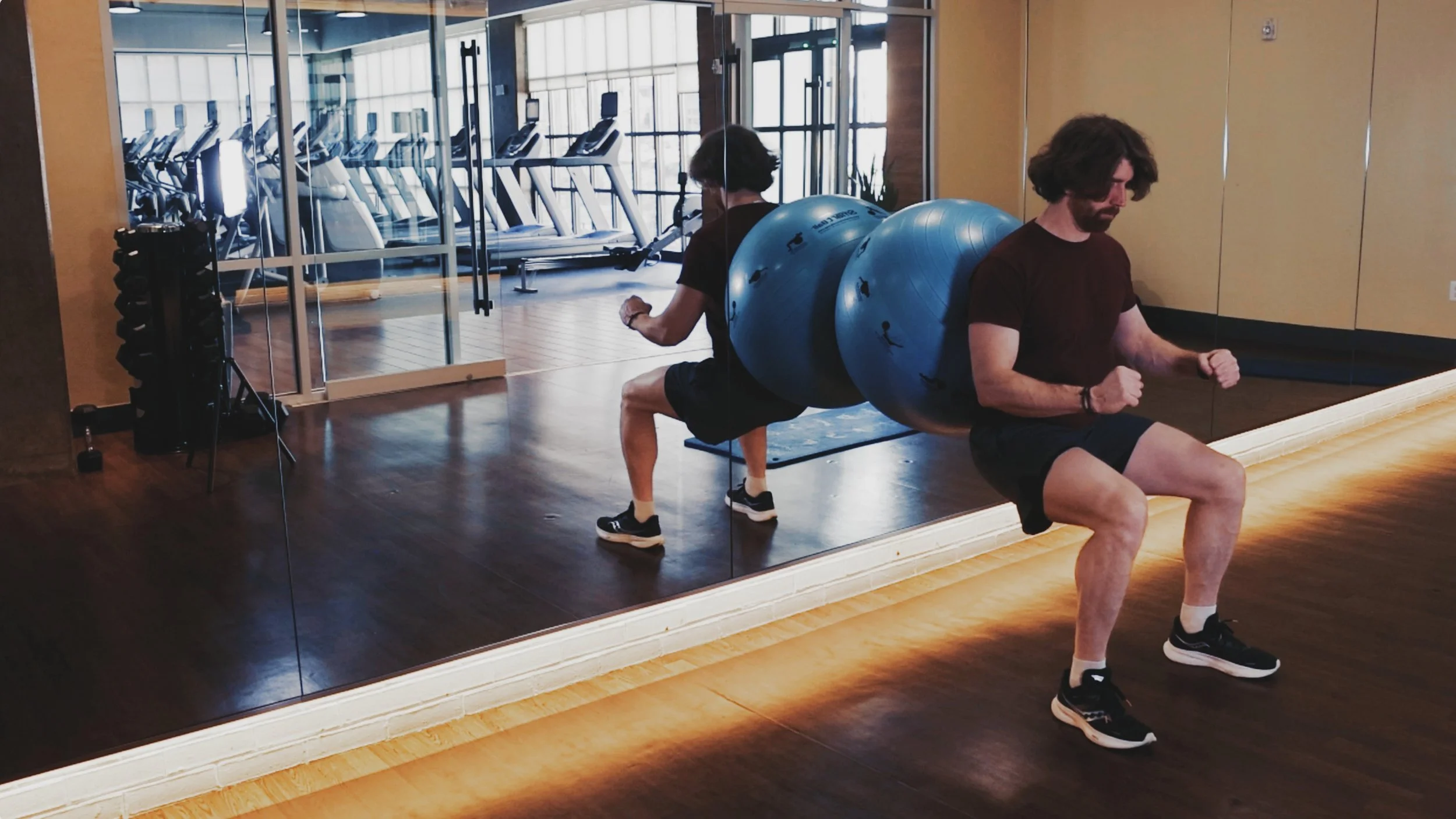 Man with beard doing squats with blue Prism Fitness Smart ball against a mirror
