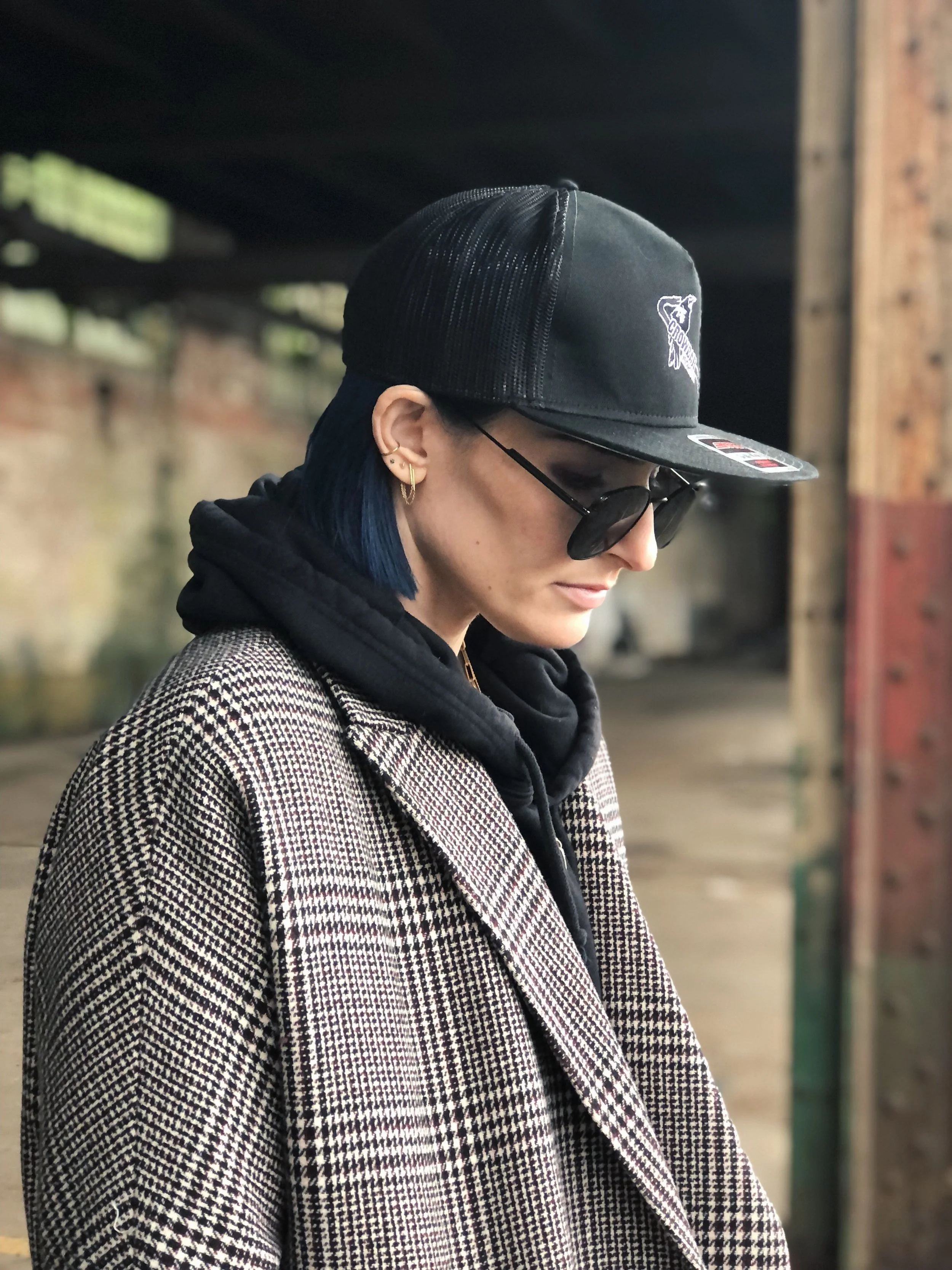 Woman with a baseball hat, dark sunglasses and a hoodie with a tweed coat.