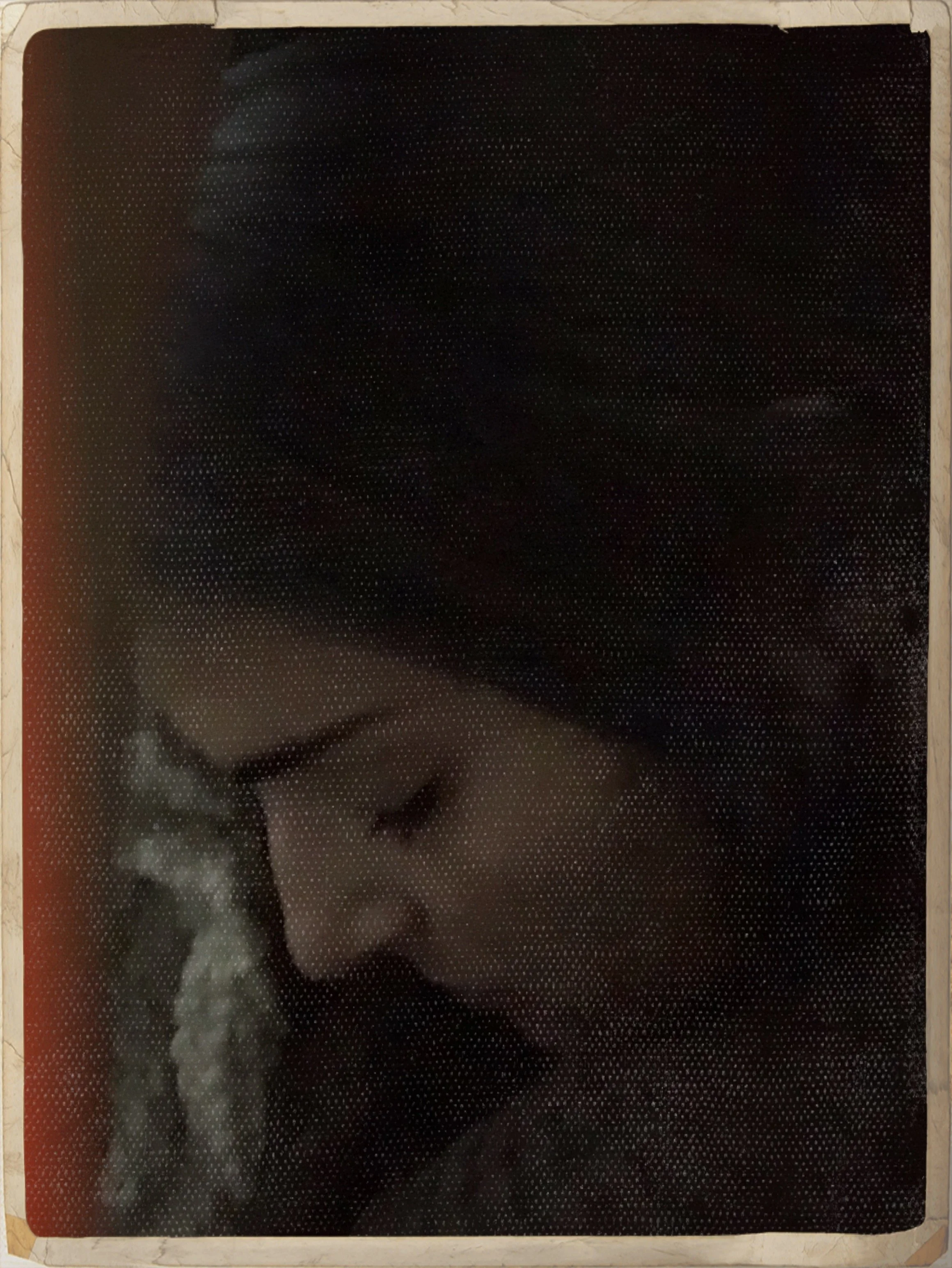 A woman with glasses and dark hair looking down, resting her head on a knitted blanket or pillow.