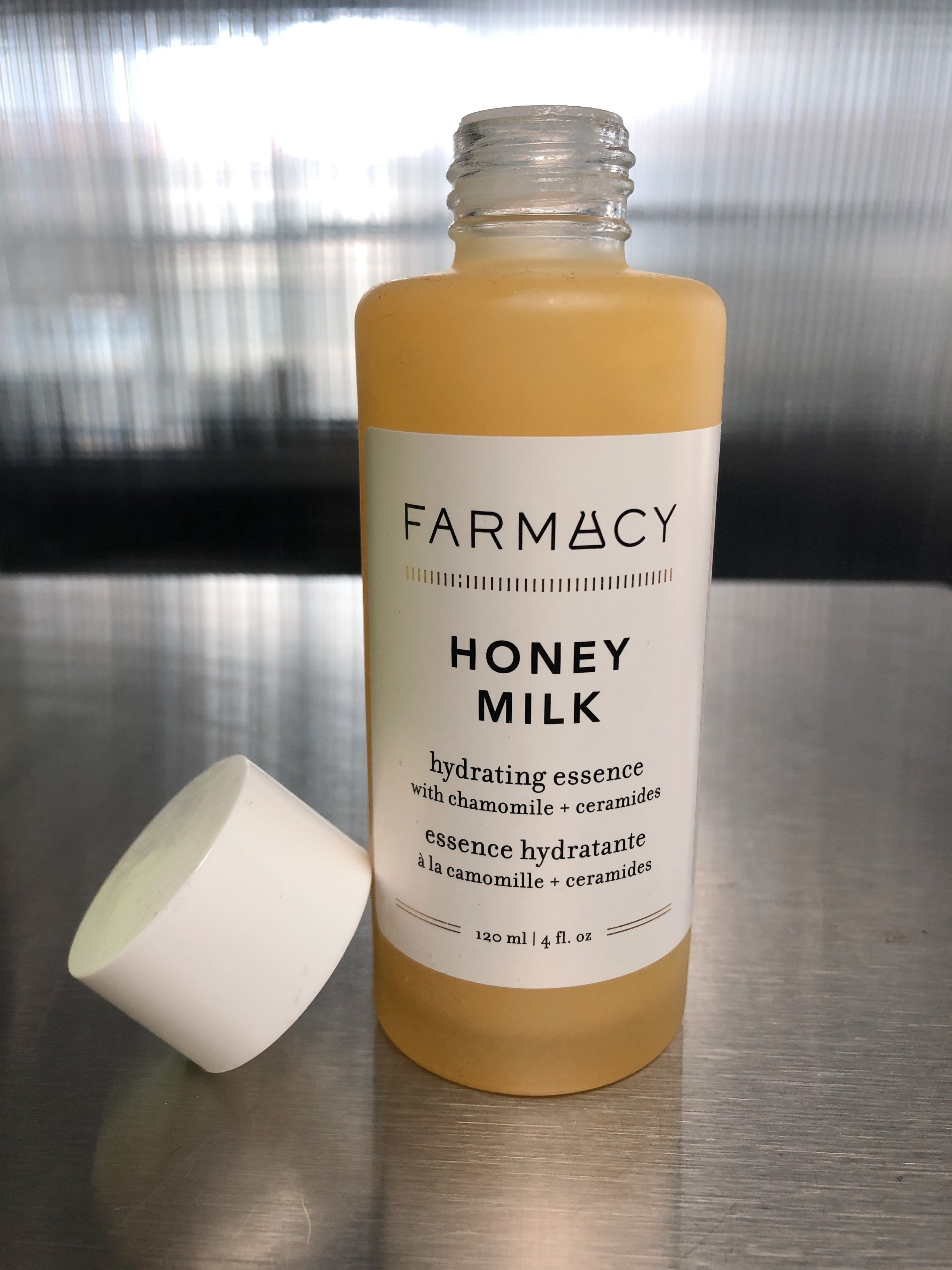 Farmacy Honey Milk Toner on a metal surface with the white cap leaning against it