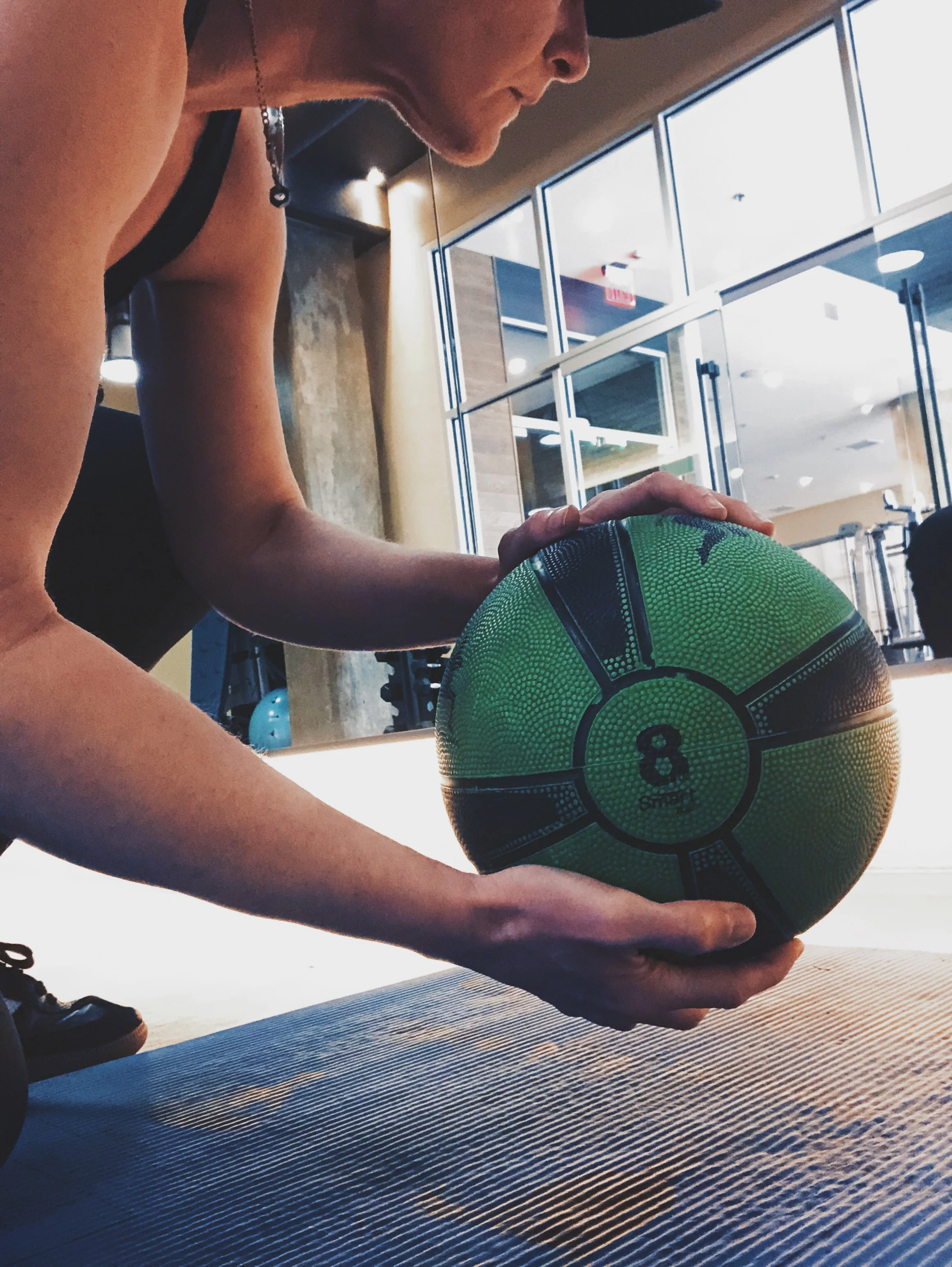 A person at a gym places a green and black medicine ball on the floor during a workout.