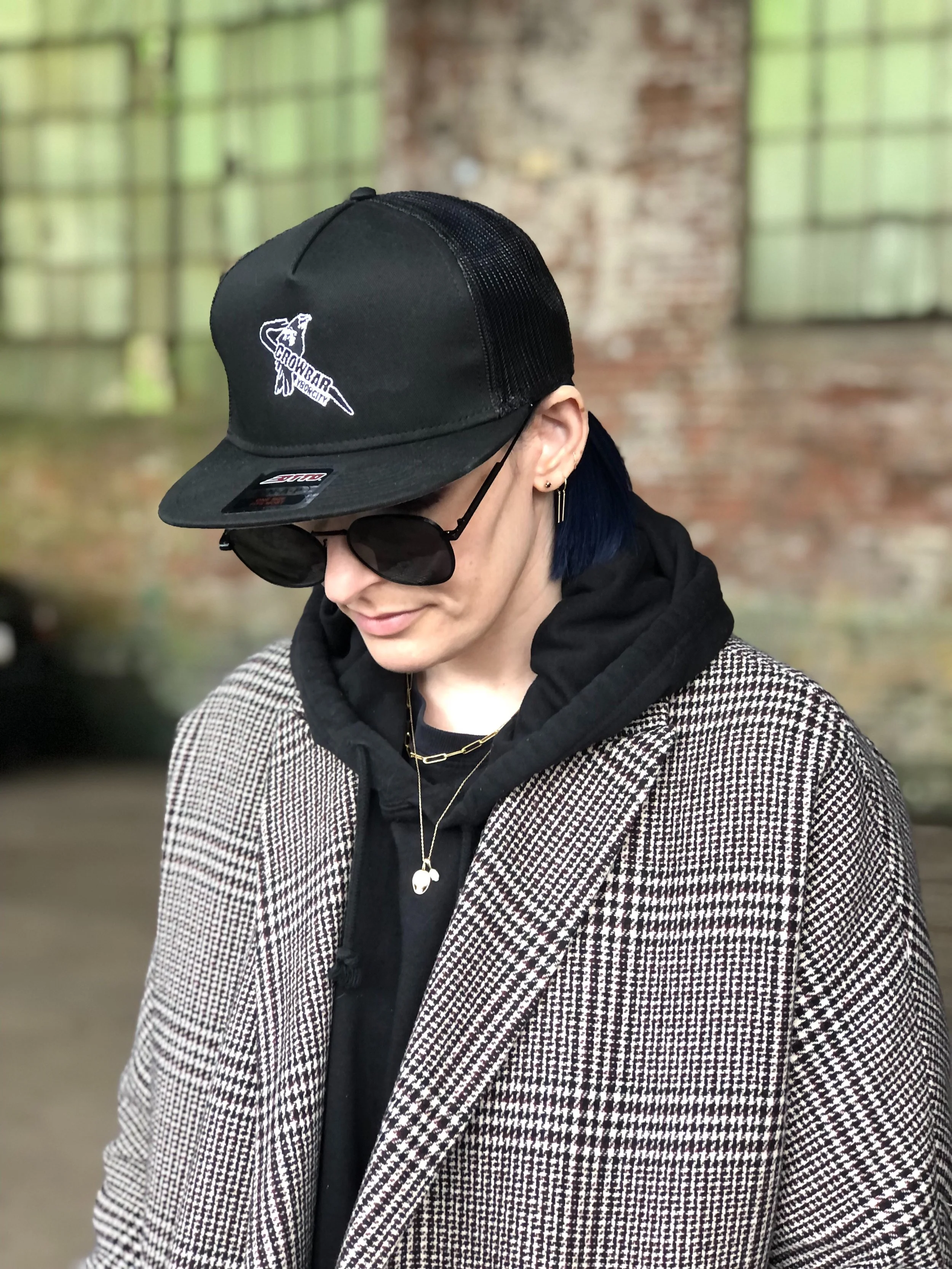 Woman with a baseball hat, dark sunglasses and a hoodie with a tweed coat.