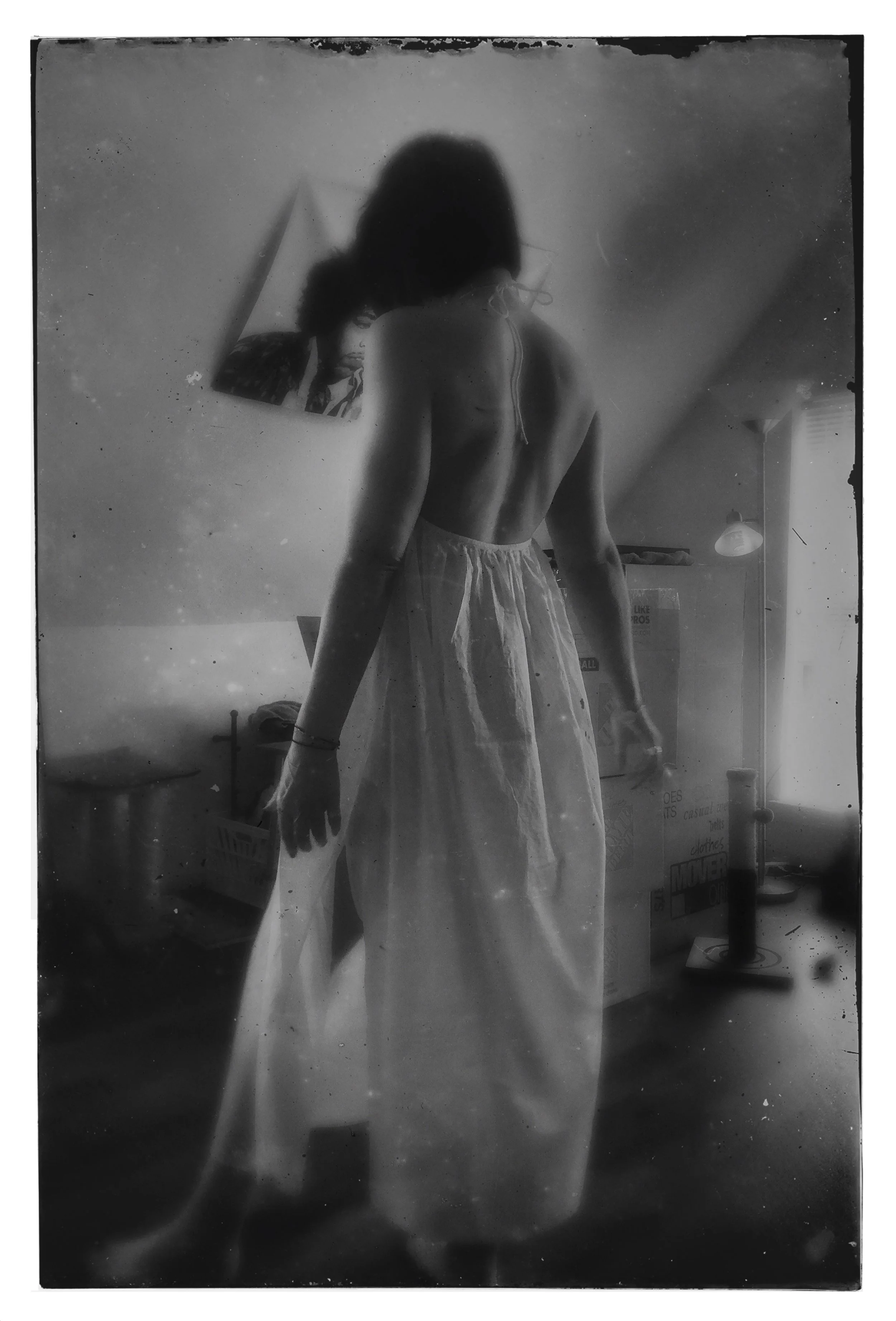 A black and white photograph of a woman in a white dress with short dark hair and back facing the camera in front of a painting of Jimi Hendrix