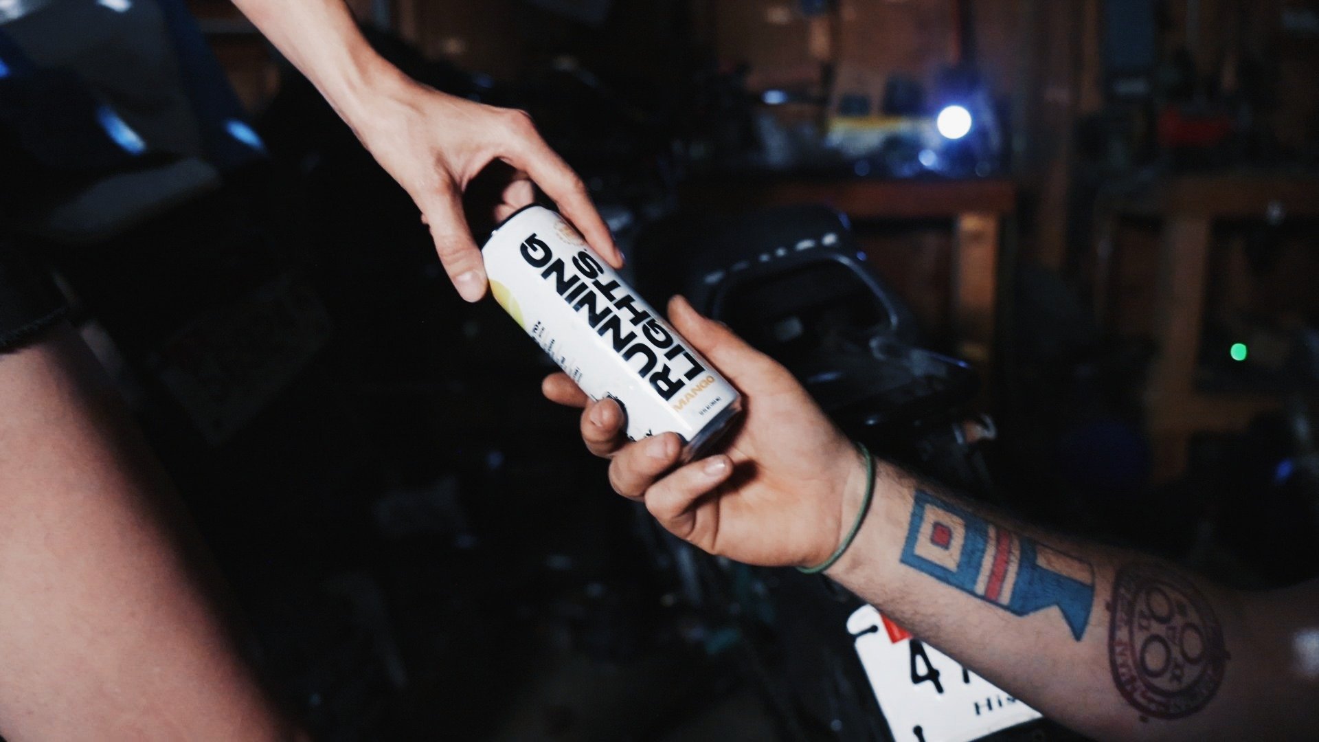 Close up of a woman handing a can of Running Lights Beverage to a man with a tattoo on his arm
