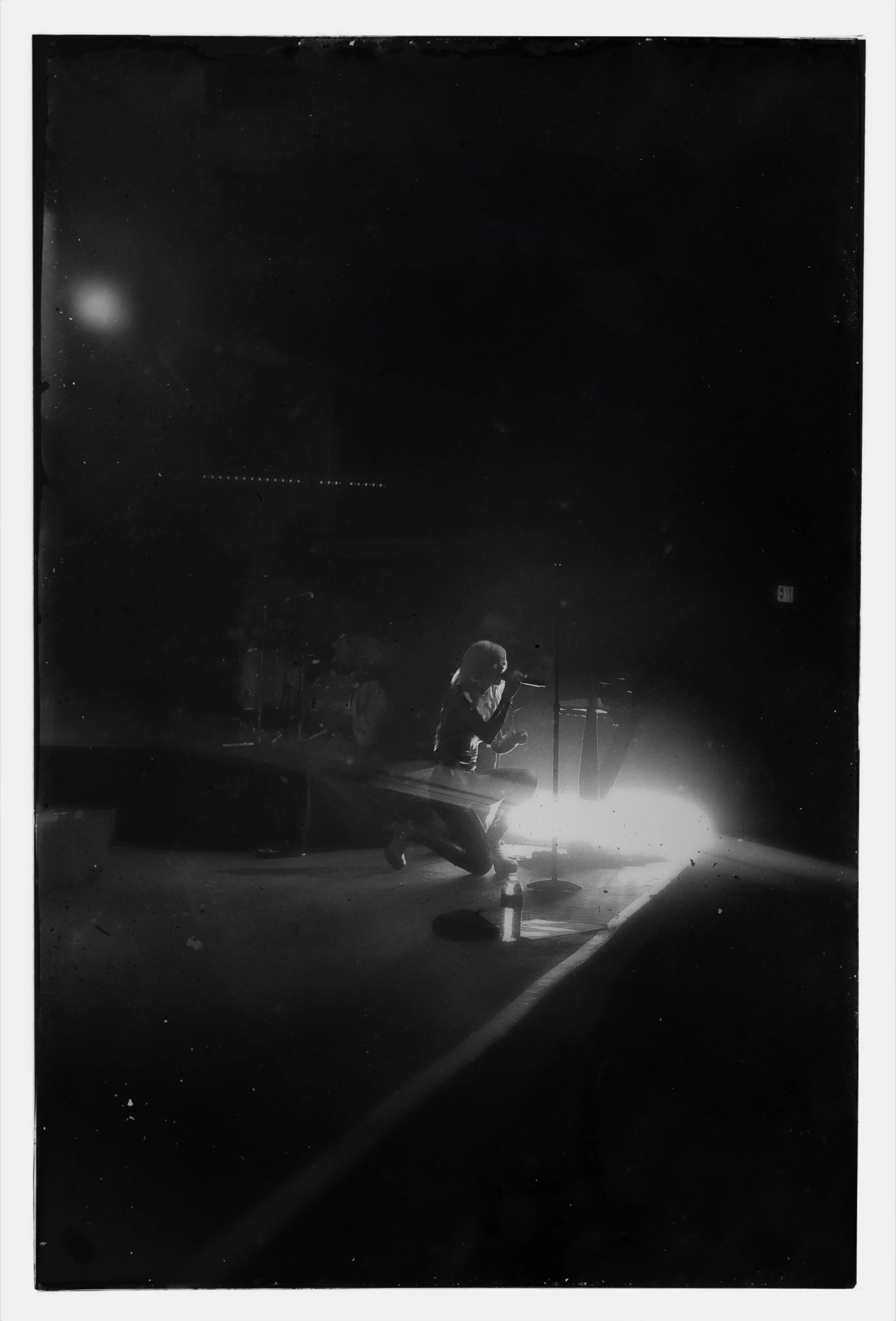 A female singer from Cannons performing on stage at 9:30 in DC kneeling on stage, singing into a microphone, with stage lights behind her creating a backlit scene in black and white.
