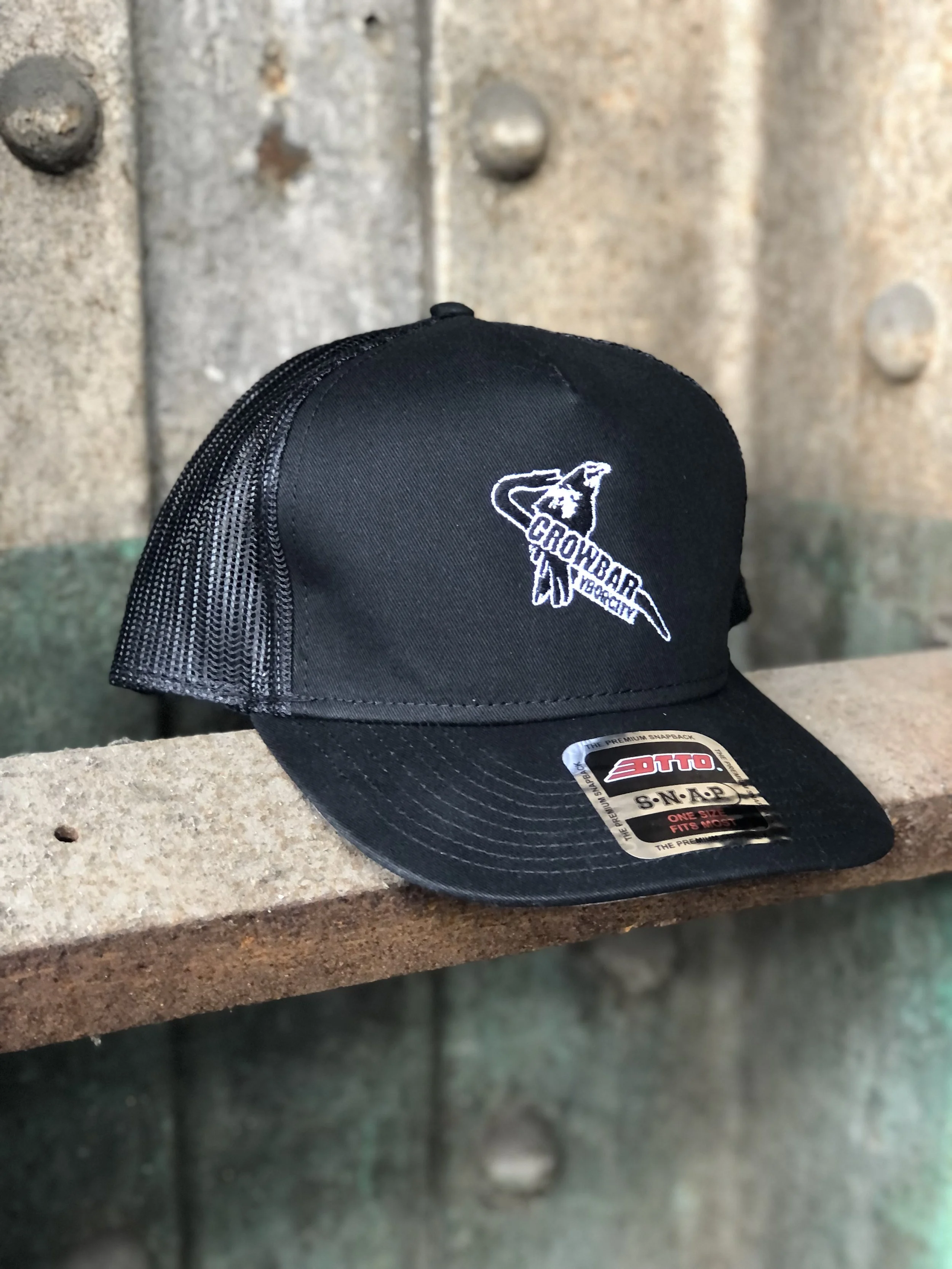 A black trucker hat with the Crowbar music venue logo on an industrial rail and metal background.