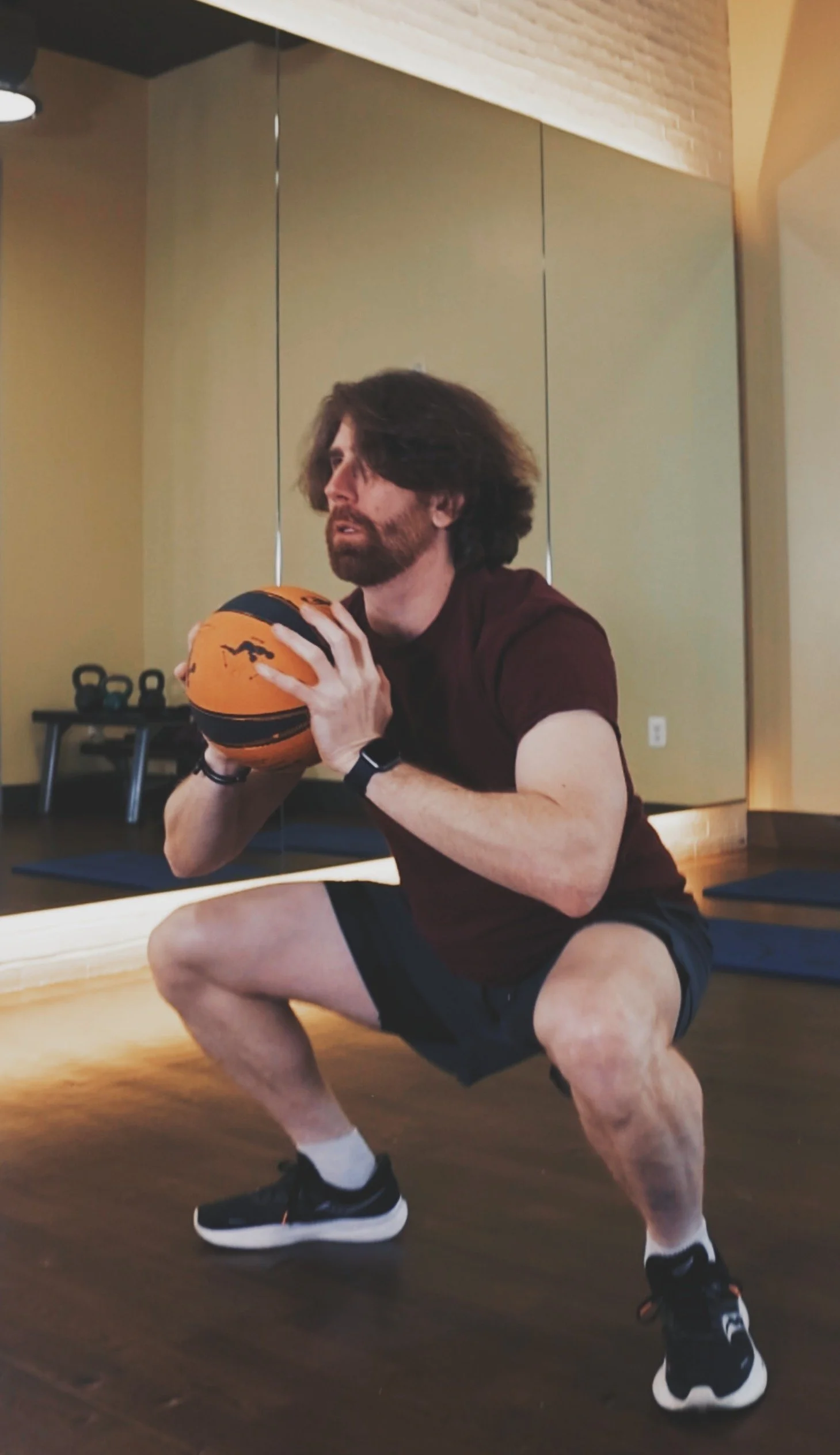 A man in workout clothes holding a basketball in a squat position in a gym room.