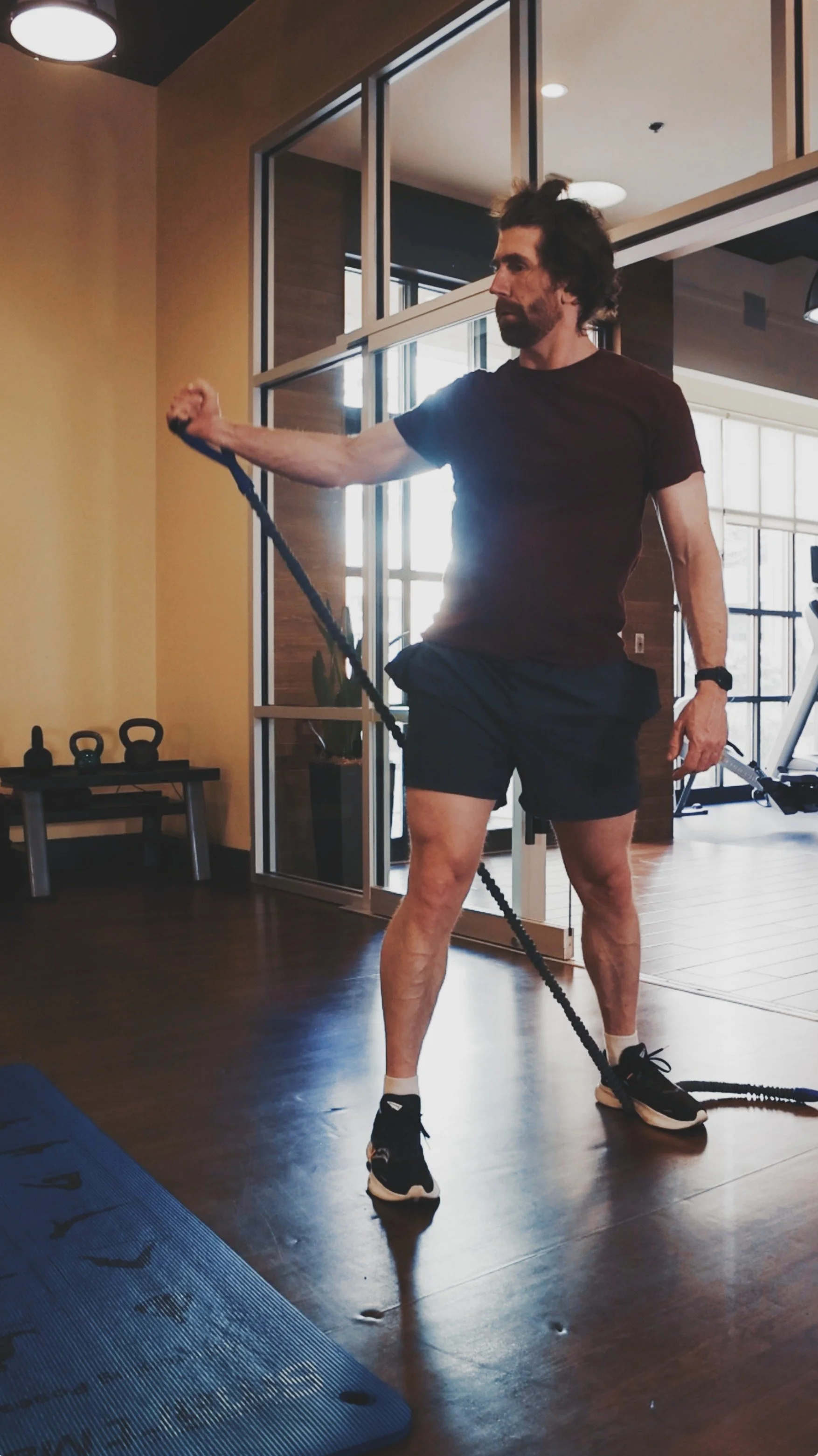 A man in black shorts and t-shirt doing exercises with a resistance band at a gym.